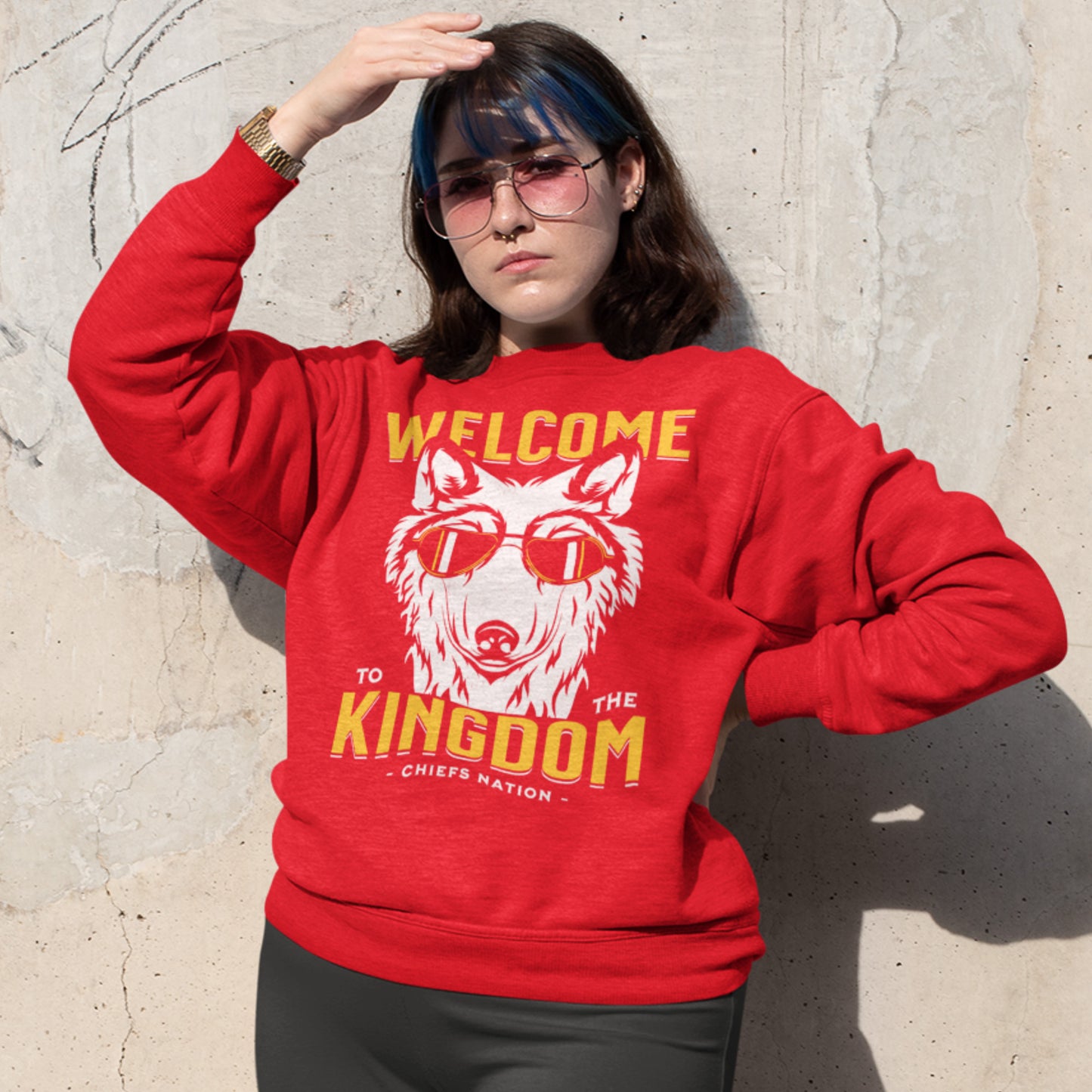 KC Swag Kansas City Chiefs Distressed White & Gold Cool Wolf Kingdom on a Red Crewneck Sweatshirt worn by a female model shading her eyes from the sun while standing in front of a concrete wall
