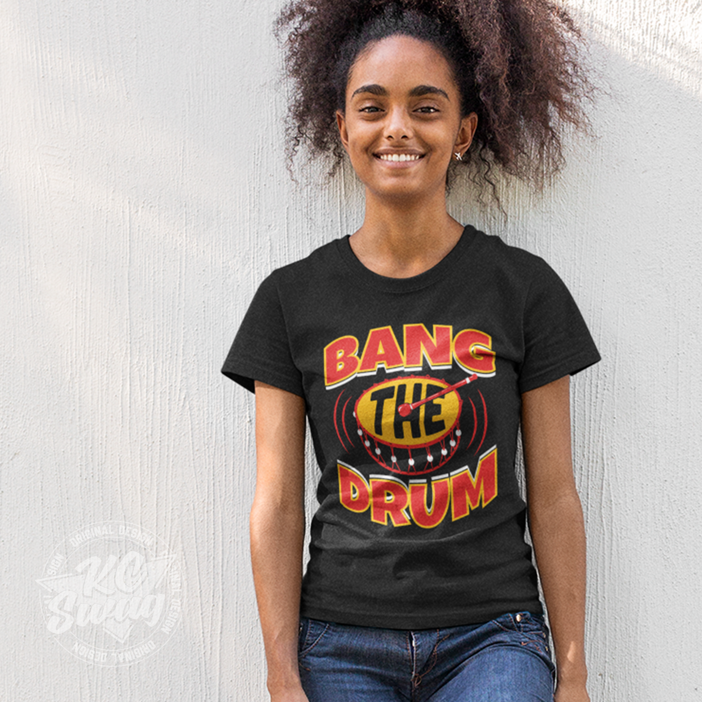 KC Swag - Kansas City Chiefs BANG THE DRUM on black unisex t-shirt worn by female model standing against a concrete wall