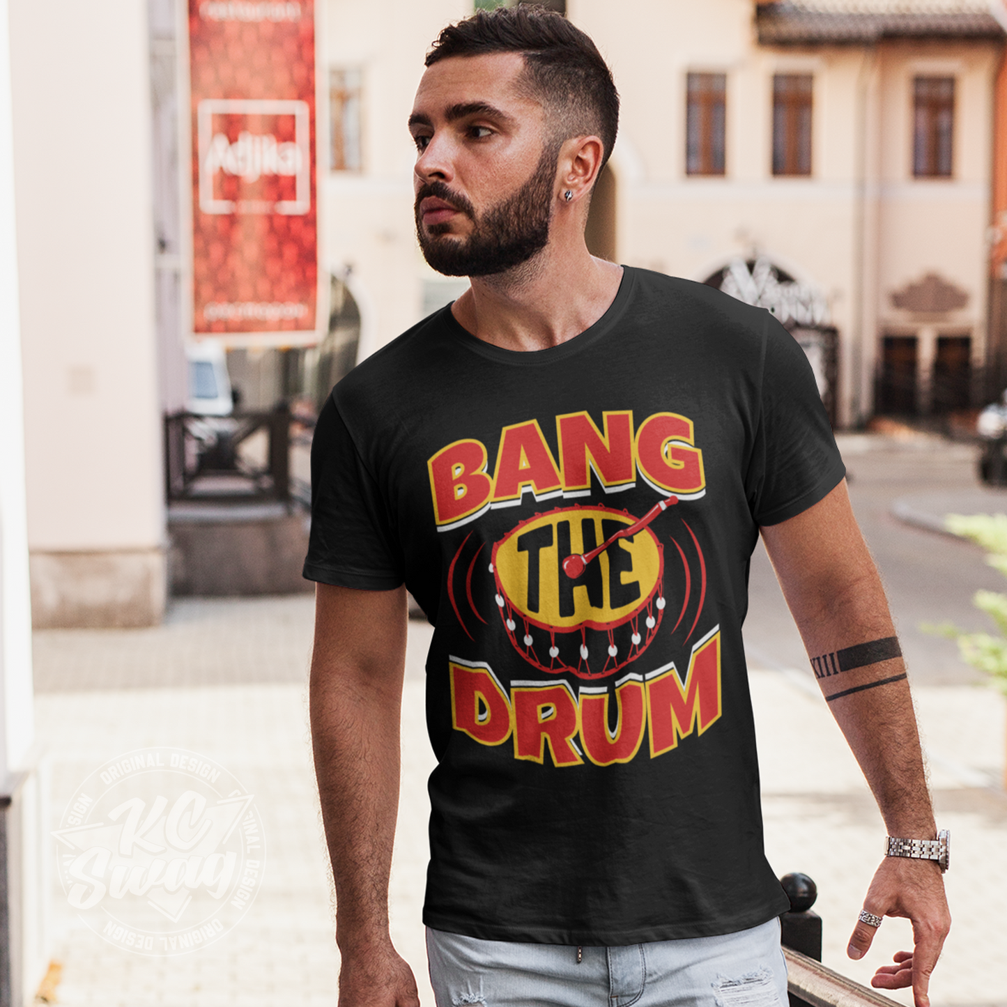 KC Swag - Kansas City Chiefs BANG THE DRUM on black unisex t-shirt worn by male model walking around an open-air plaza