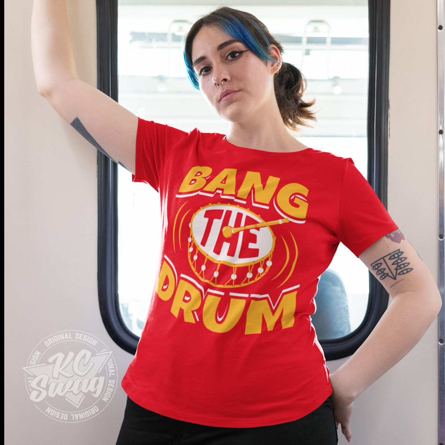 KC Swag - Kansas City Chiefs BANG THE DRUM on red unisex t-shirt worn by female model standing by window in a streetcar