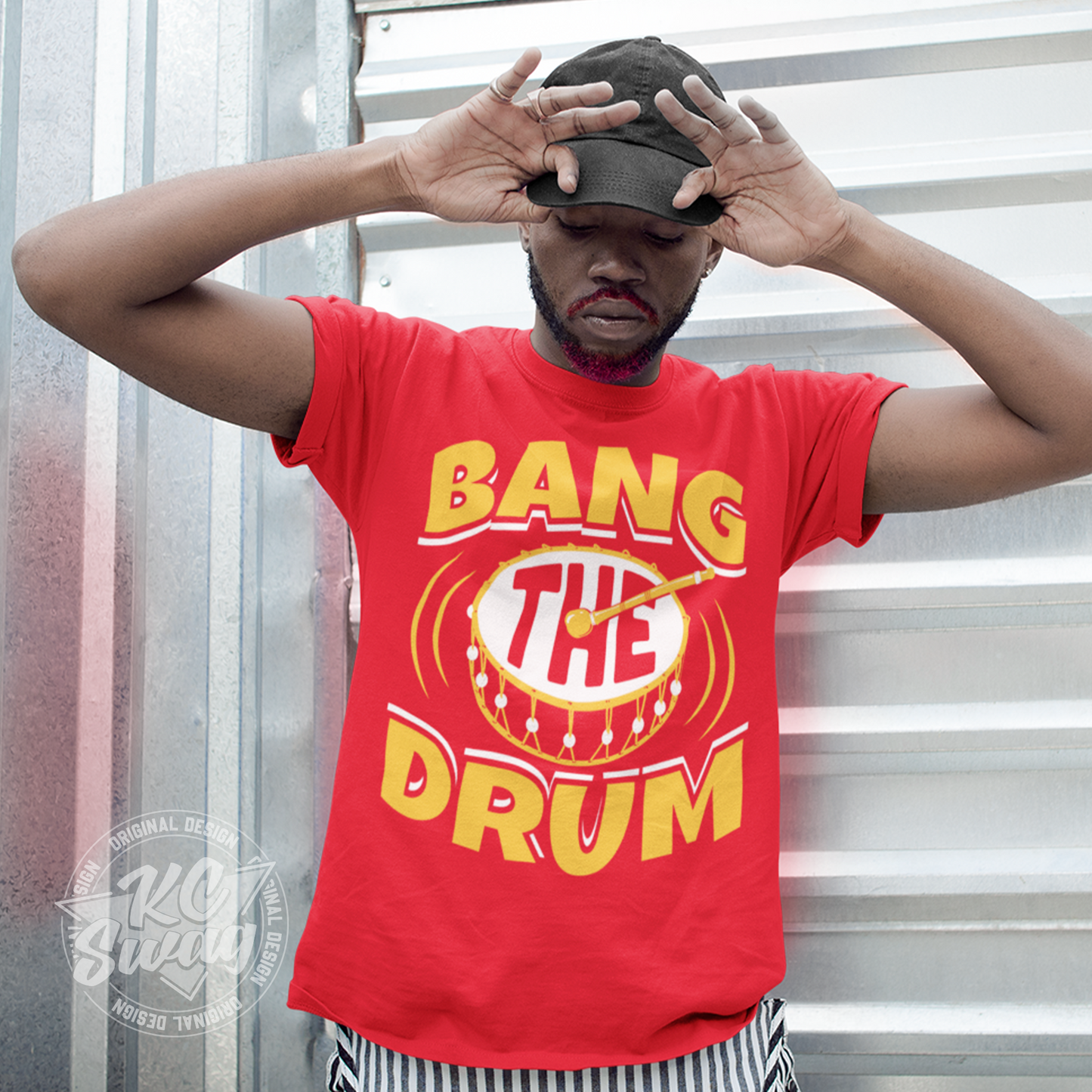 KC Swag - Kansas City Chiefs BANG THE DRUM on red unisex t-shirt worn by male model standing in front of a metal garage door wearing a black baseball cap