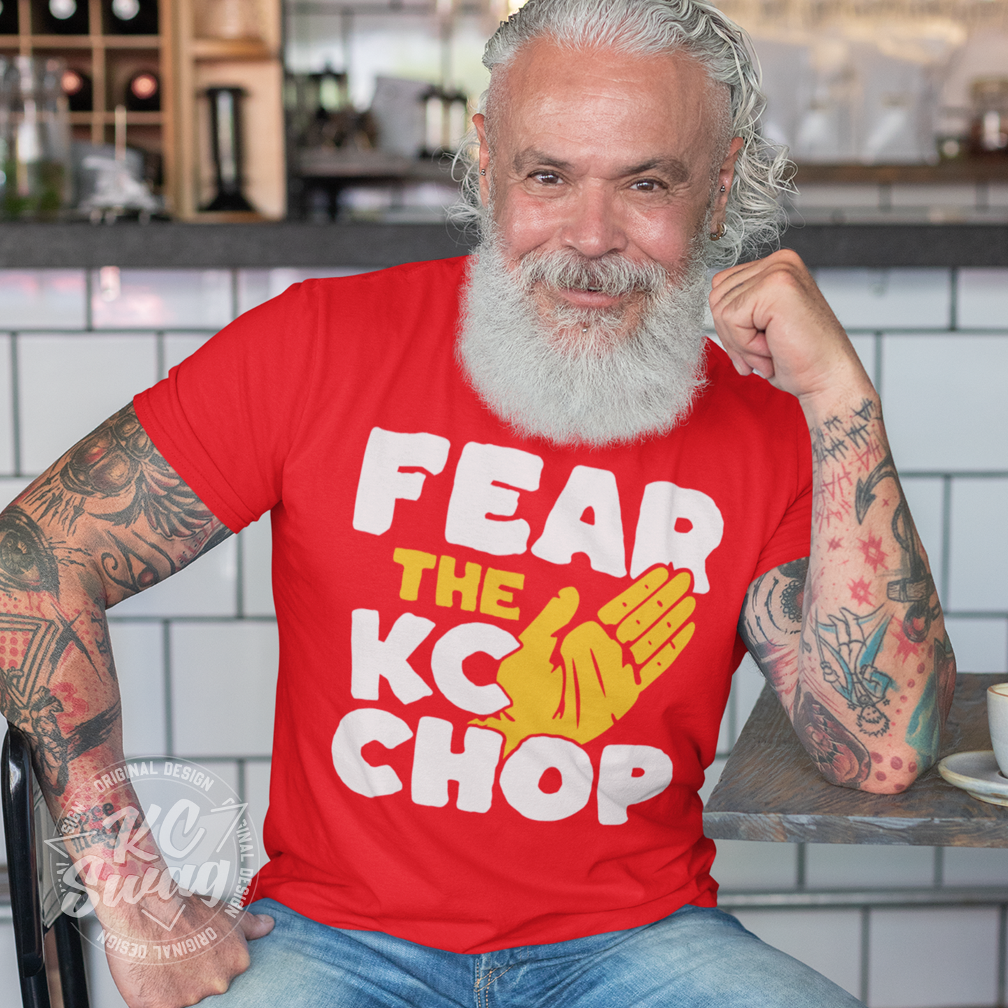 KC Swag - Kansas City Chiefs FEAR THE TOMAHAWK KC CHOP on red unisex t-shirt worn by bearded male model sitting at table in a moder cafe