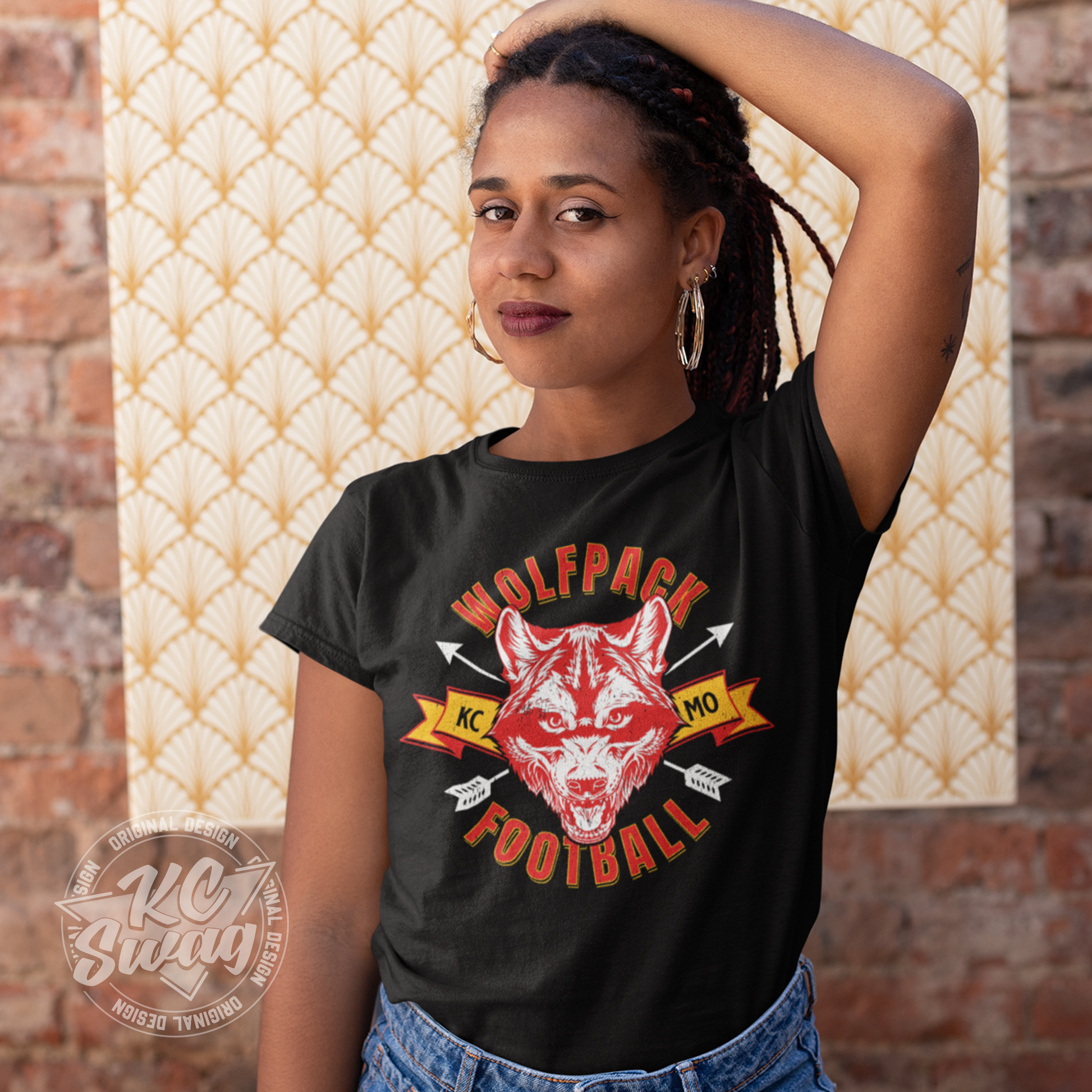 KC Swag - Kansas City Chiefs WOLFPACK FOOTBALL KCMO on black unisex t-shirt worn by female model stanging in front of a patterned canvas on a brick wall