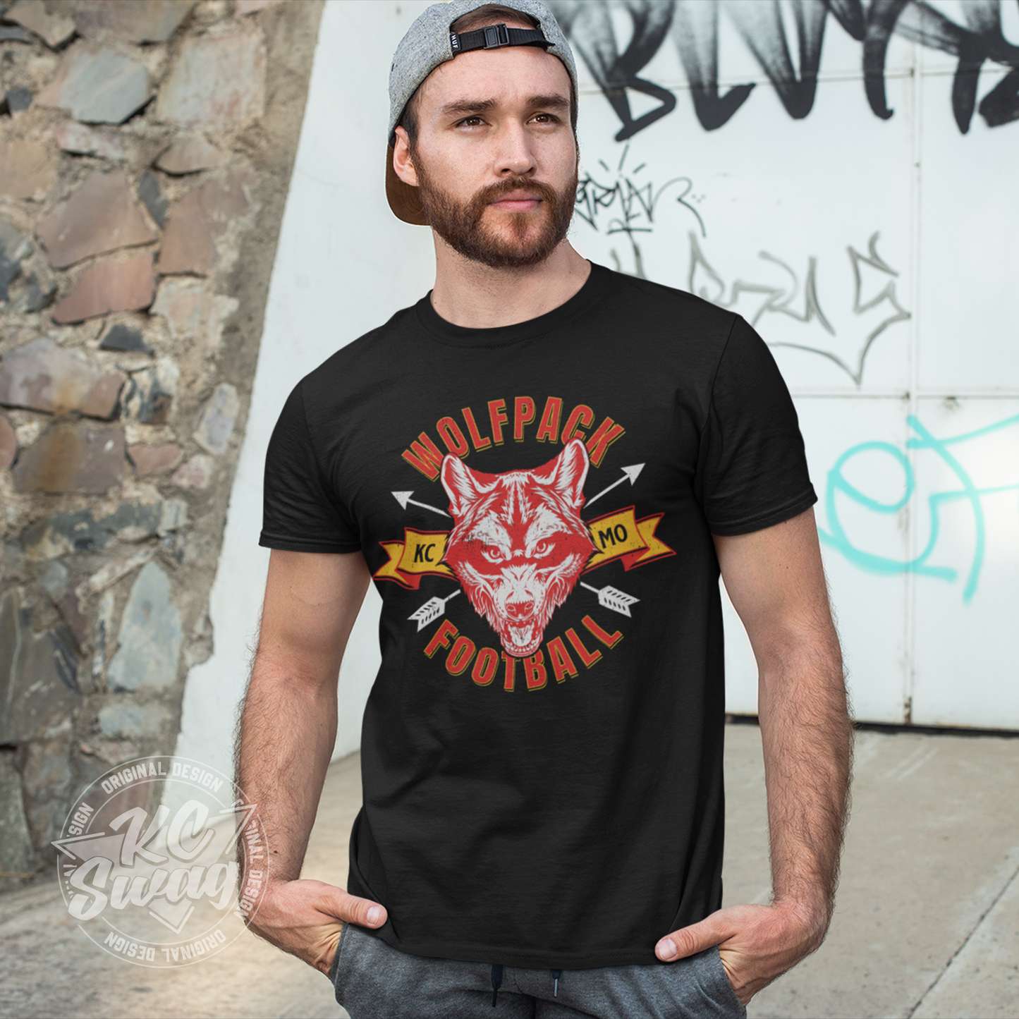 KC Swag - Kansas City Chiefs WOLFPACK FOOTBALL KCMO on black unisex t-shirt worn by male model standing in front of a graffitied wall in public park