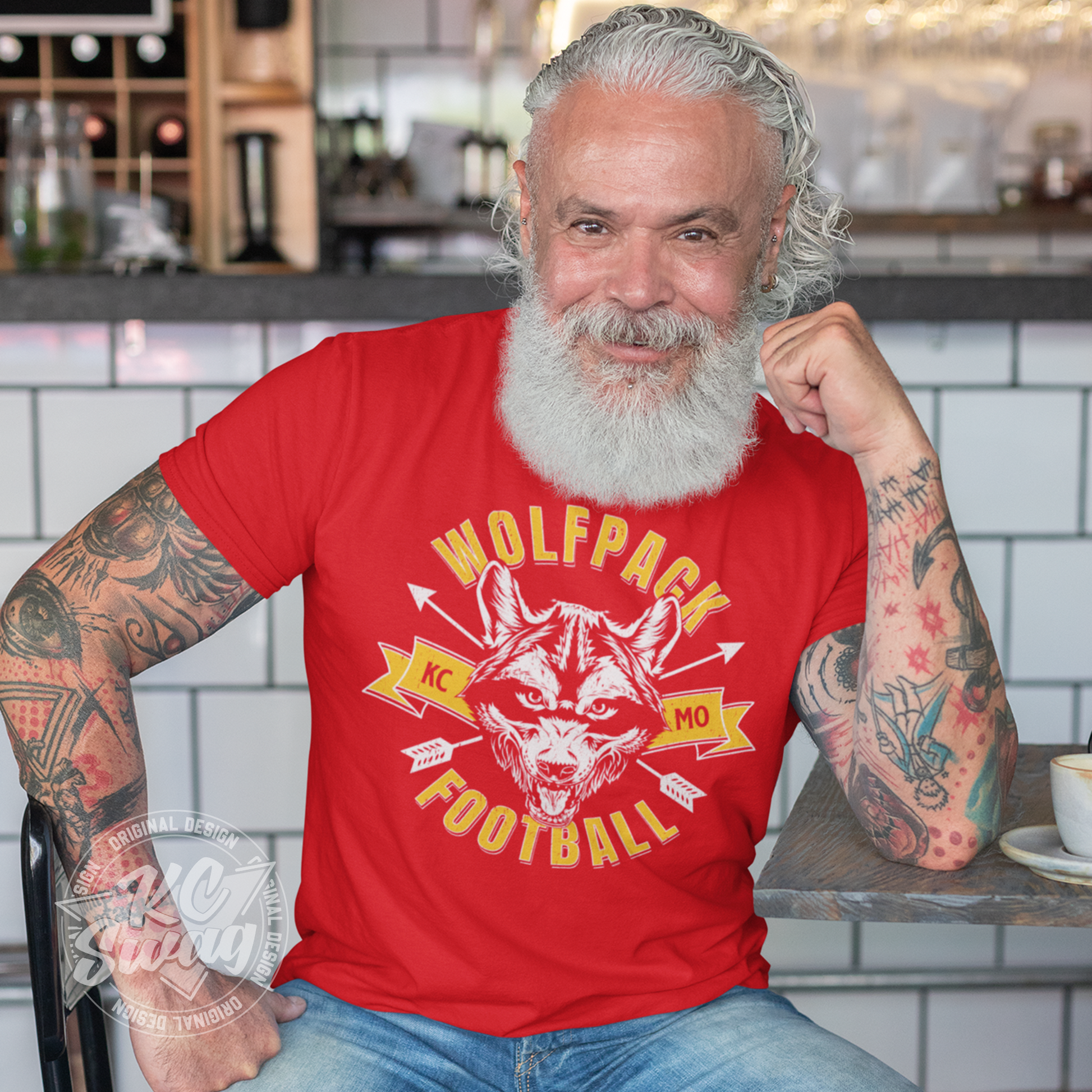 KC Swag - Kansas City Chiefs WOLFPACK FOOTBALL KCMO on red unisex t-shirt worn by bearded male model sitting at table in a modern cafe