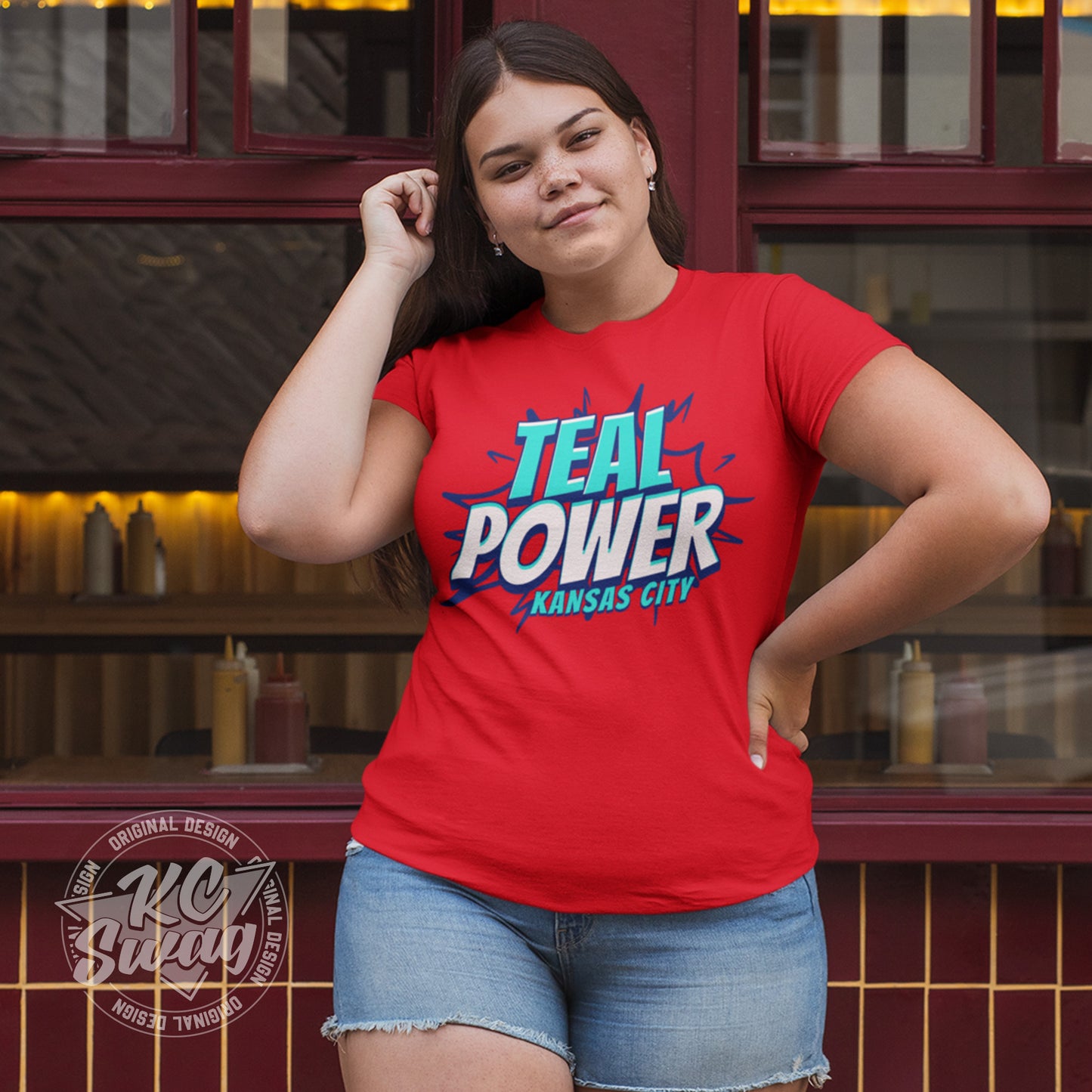 KC Swag - Kansas City Current, Teal Power KC design on red unisex t-shirt worn by female model standing outside of a restaurant