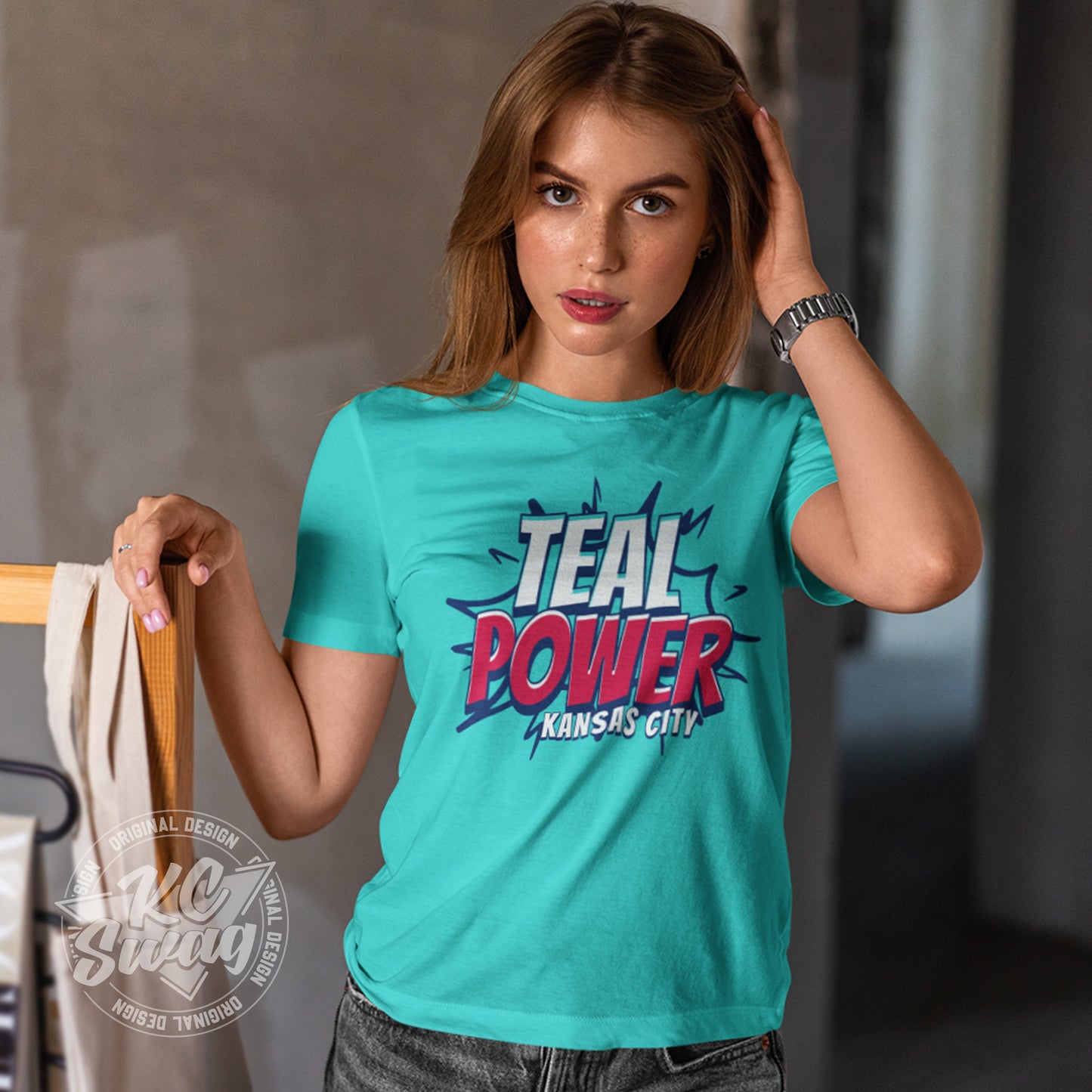 KC Swag - Kansas City Current, Teal Power KC design on teal unisex t-shirt worn by female model leaning on wooden clothes rack in a studio setting