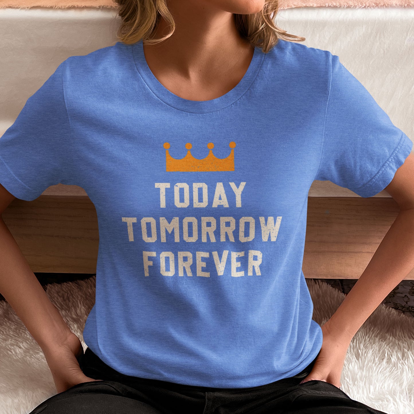 kc swag, kansas city royals, heather columbia blue unisex t-shirt featuring a gold crown above white text that says "Today, Tomorrow, Forever" with a distressed, worn-out look, worn by a female model sitting in a bedroom with her hands on her hips