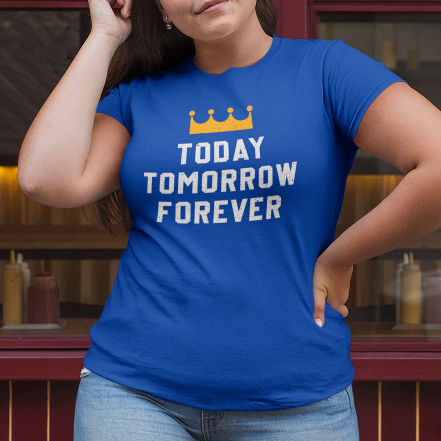 kc swag, kansas city royals, royal blue unisex t-shirt featuring a gold crown above white text that says "Today, Tomorrow, Forever" with a distressed, worn-out look, worn by a female model standing outside of restaurant windows