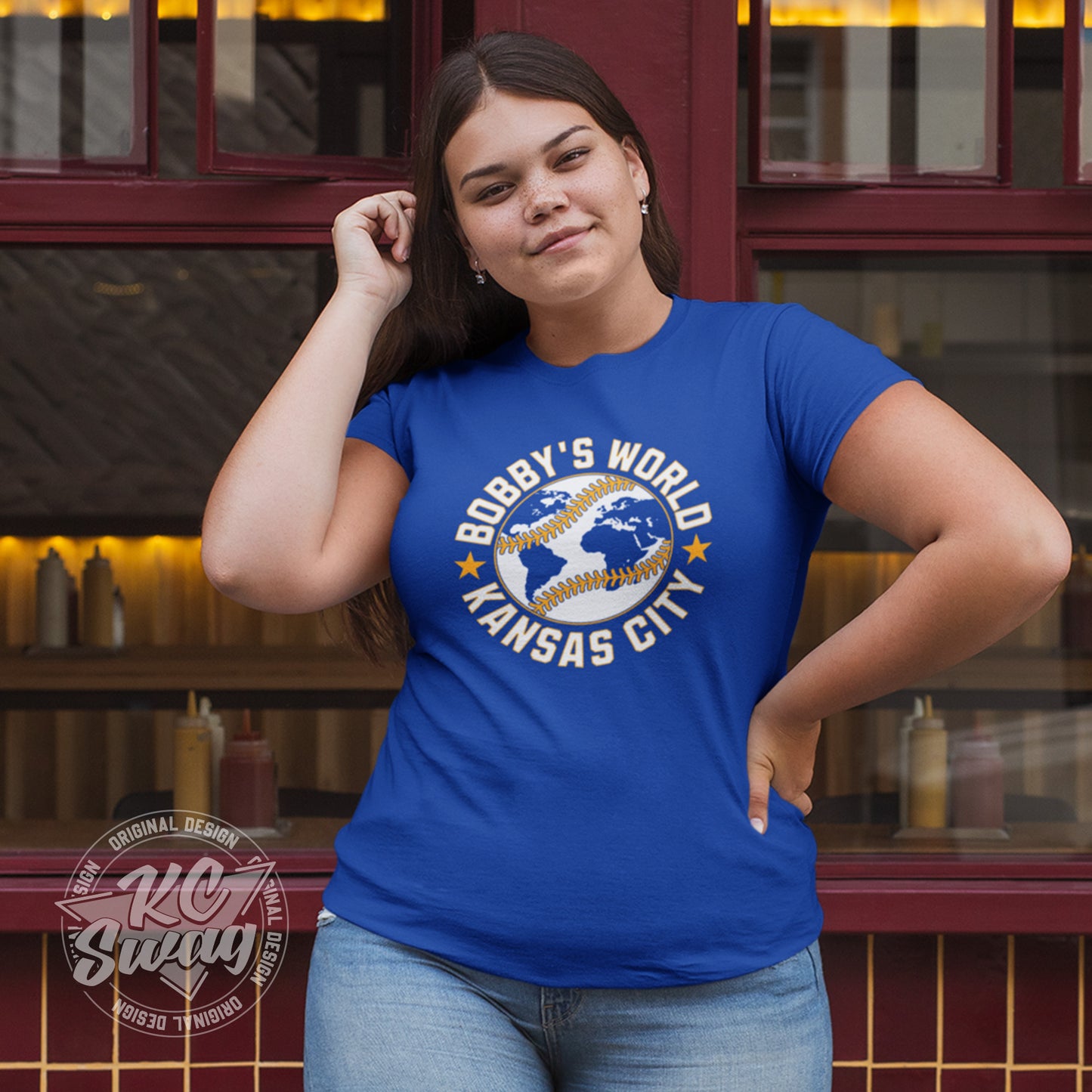 KC Swag - Kansas City Royals, Bobby's World design on royal blue unisex t-shirt worn by female model standing on sidewalk outside restaurant windows