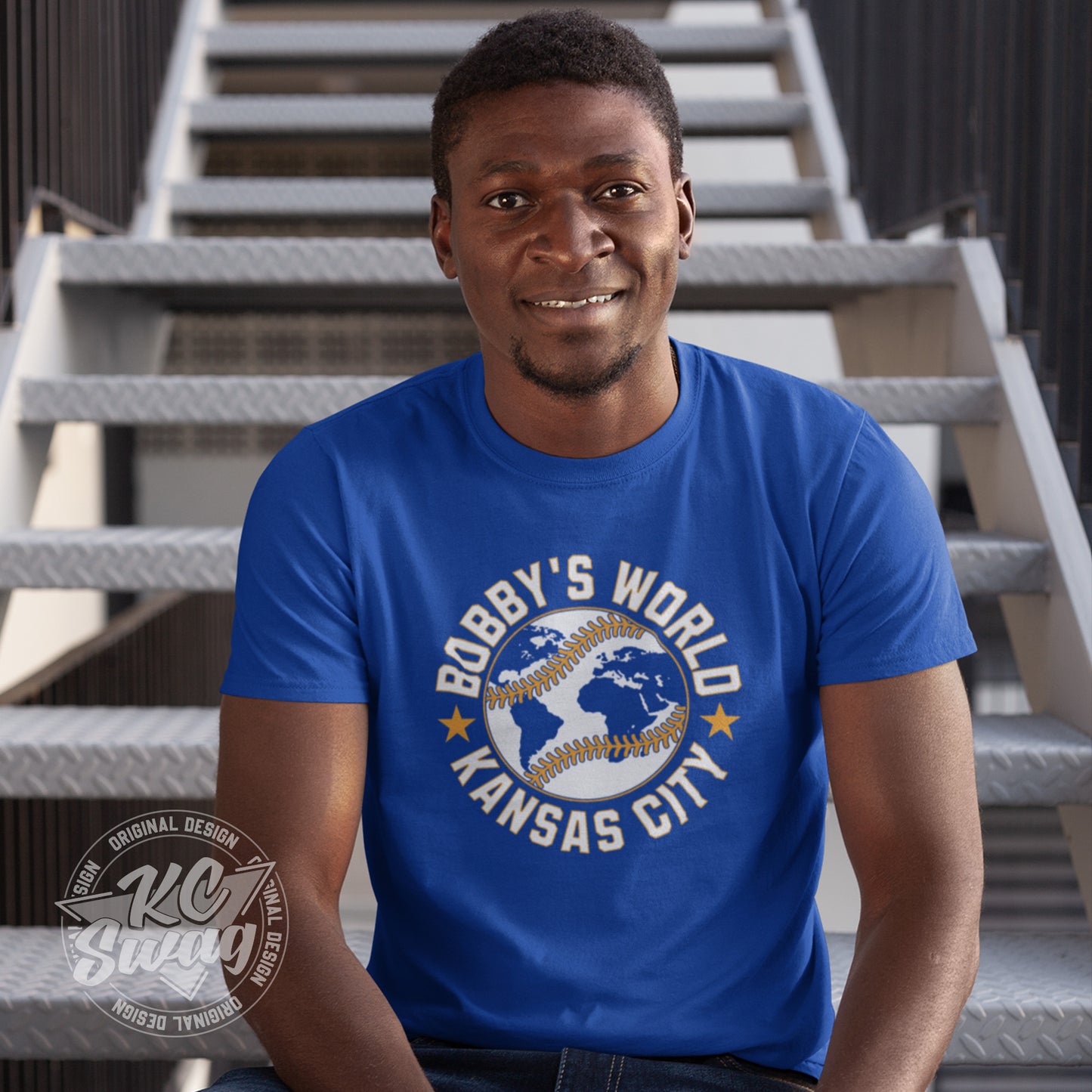 KC Swag - Kansas City Royals, Bobby's World design on royal blue unisex t-shirt worn by male model sitting on a metal staircase