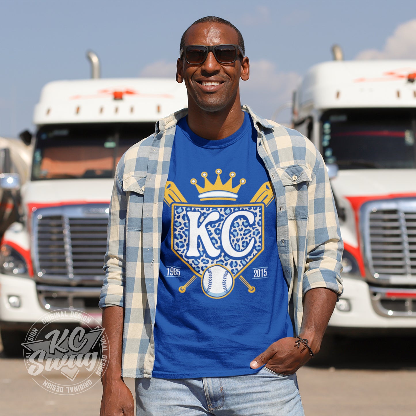 KC Swag - Kansas City Royals, Cheetah Home Plate design on royal blue unisex t-shirt worn by male model under an open plaid shirt standing outside in front of a line of semi trucks