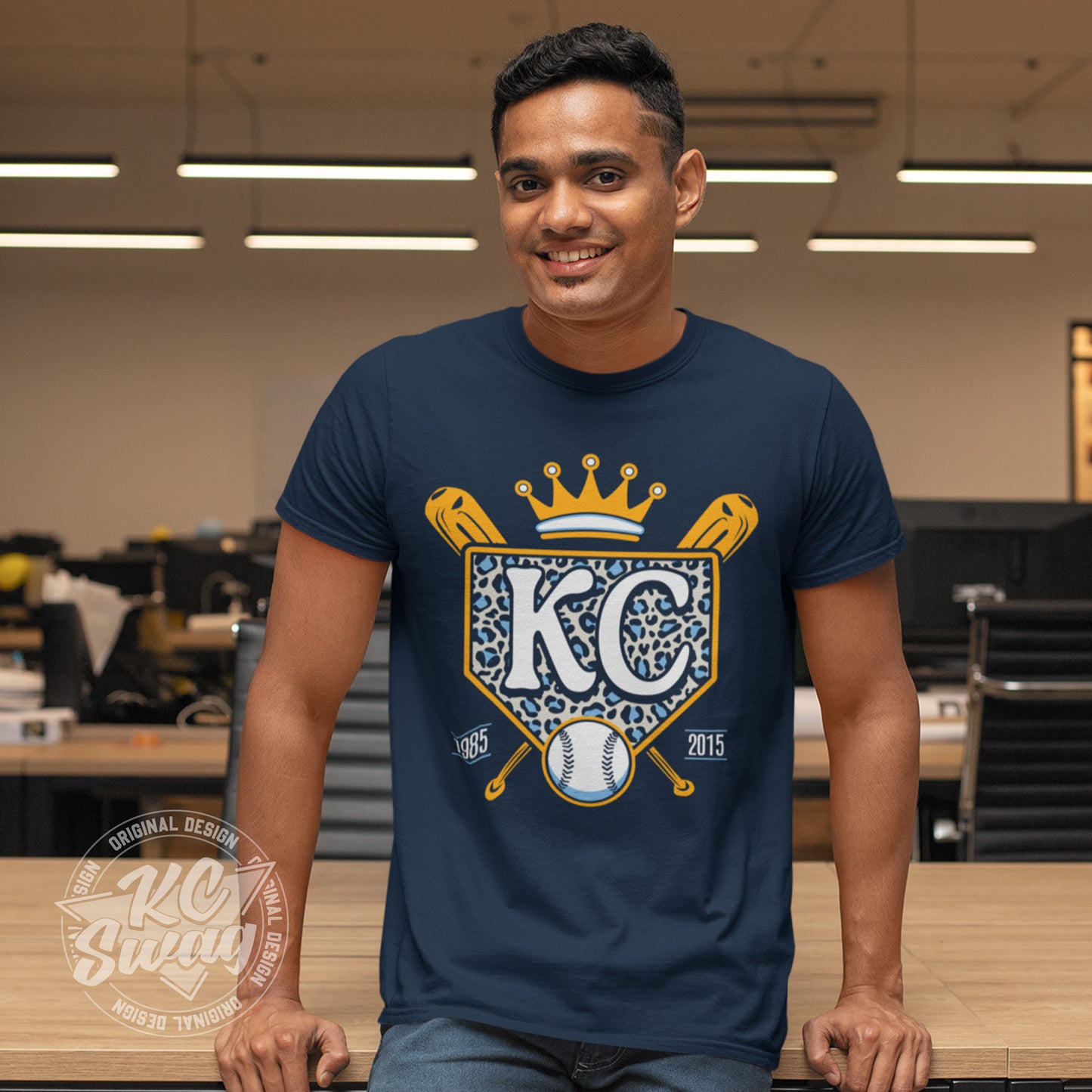 KC Swag - Kansas City Royals, Cheetah Home Plate design on navy blue unisex t-shirt worn by male model sitting on community table in a classroom