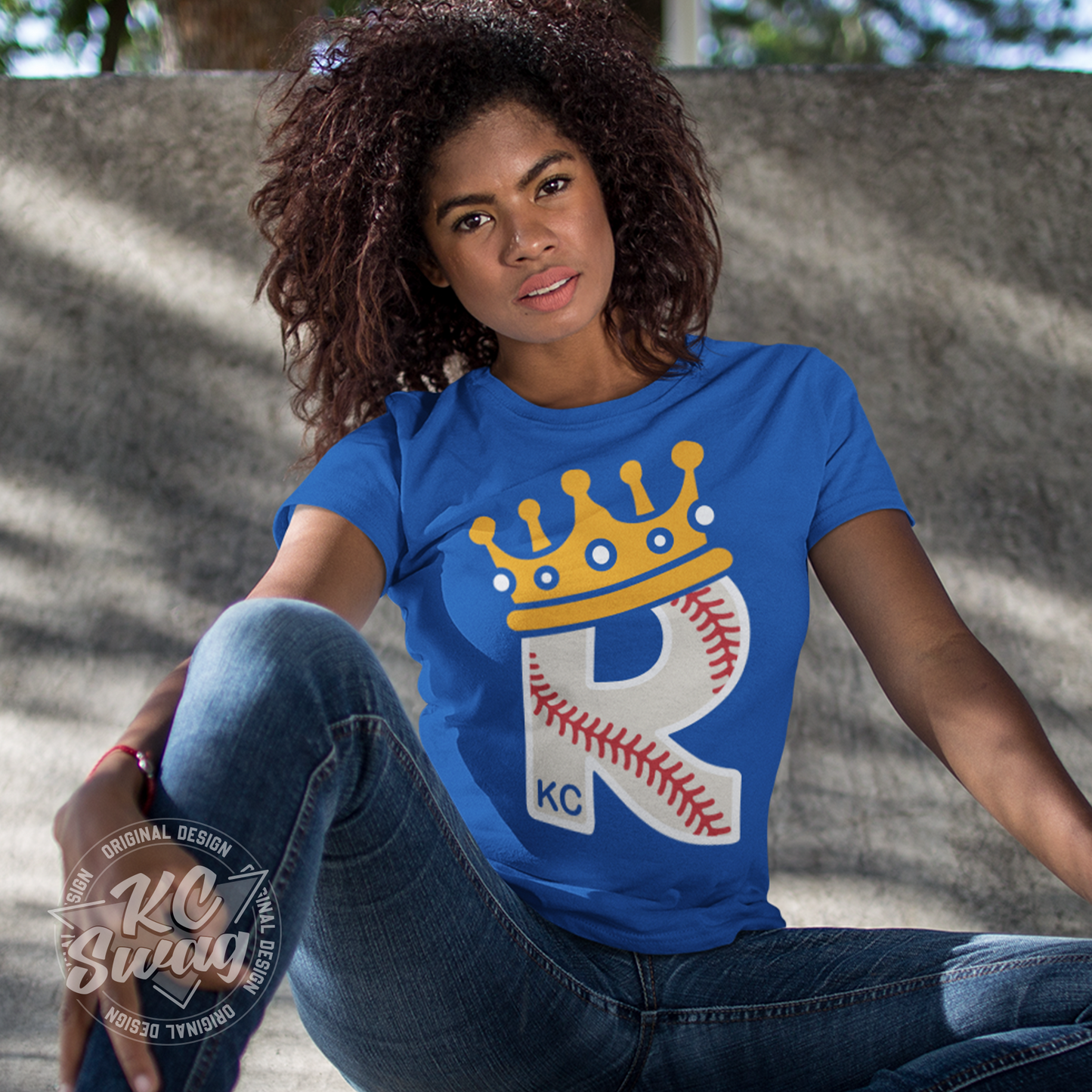 KC Swag - Kansas City Royals CROWN R-BALL KC on true royal blue unisex t-shirt worn by female model sitting in front of a concrete wall in a public park
