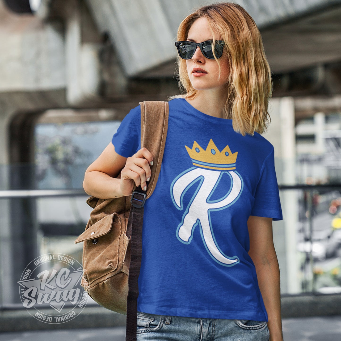 KC Swag - Kansas City Royals, Crown R design on royal blue unisex t-shirt worn by female model carrying a backpack slung over her shoulder in an urban setting