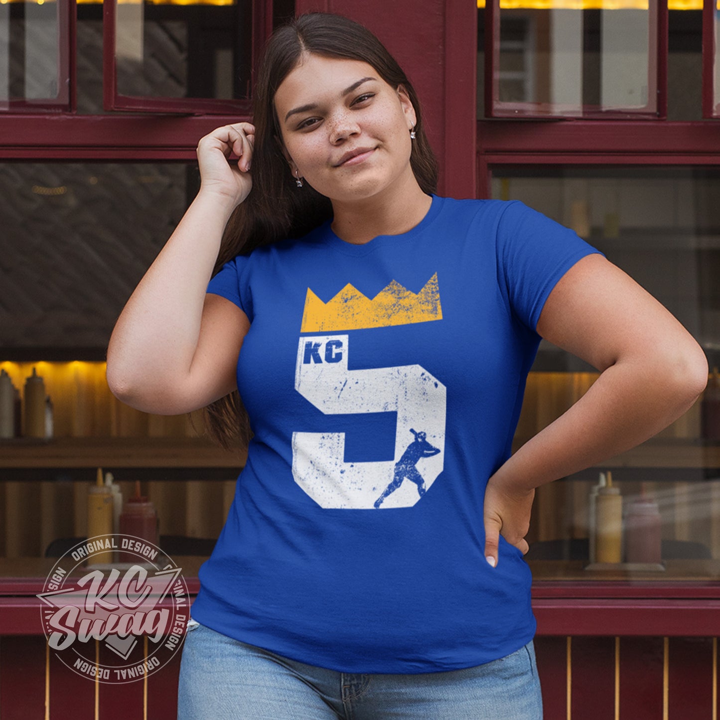 KC Swag - Kansas City Royals, Brett Five Crown design on royal blue unisex t-shirt worn by female model standing outside restaurant windows