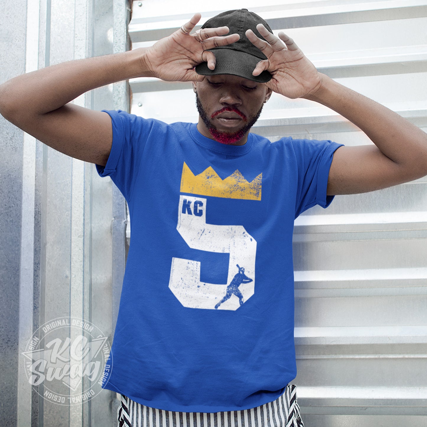 KC Swag - Kansas City Royals, Brett Five Crown design on royal blue unisex t-shirt worn by male model standing in front of a metal garage door
