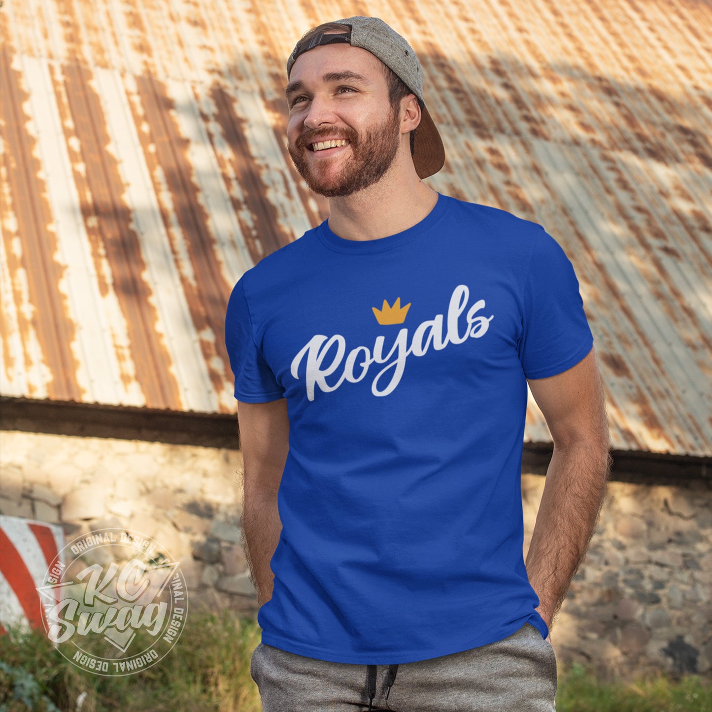 KC Swag - Kansas City Royals, FRoyals Flower Crown design on royal blue unisex t-shirt worn by male model standing in front of a rustic barn with a backwards ball cap