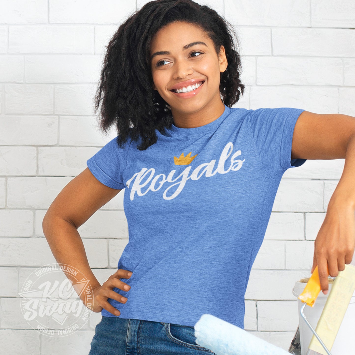 KC Swag - Kansas City Royals, FRoyals Flower Crown design on heather columbia blue unisex t-shirt worn by female model leaning on a ladder holding a paint roller in front of a white brick wall