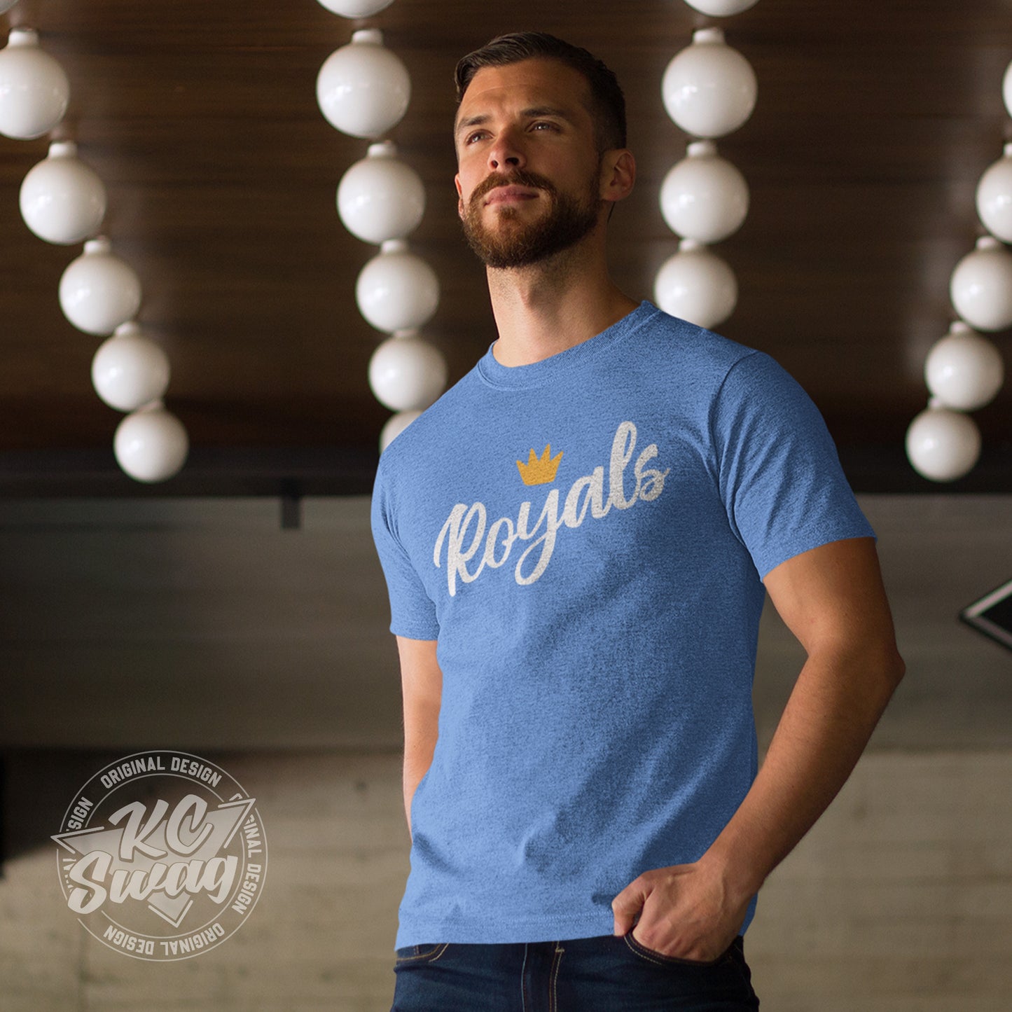 KC Swag - Kansas City Royals, FRoyals Flower Crown design on heather columbia blue unisex t-shirt worn by male model standing in a room with white light fixtures on ceiling