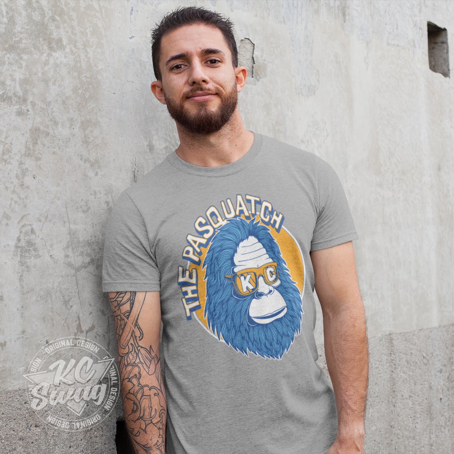 KC Swag - Kansas City Royals, Shaded KC Pasquatch on athletic heather grey unisex t-shirt worn by male model leaning on a concrete wall