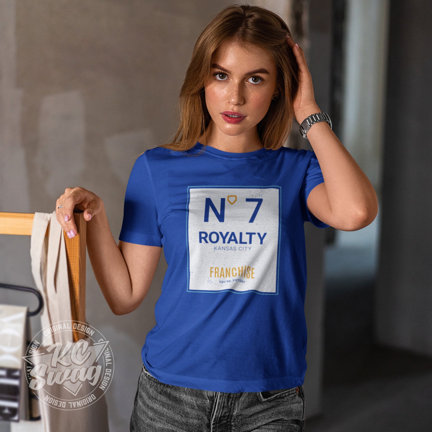 KC Swag - Kansas City Royals, Royalty Number 7 Franchise design on royal blue unisex t-shirt worn by female model leaning on clothing rack in a studio