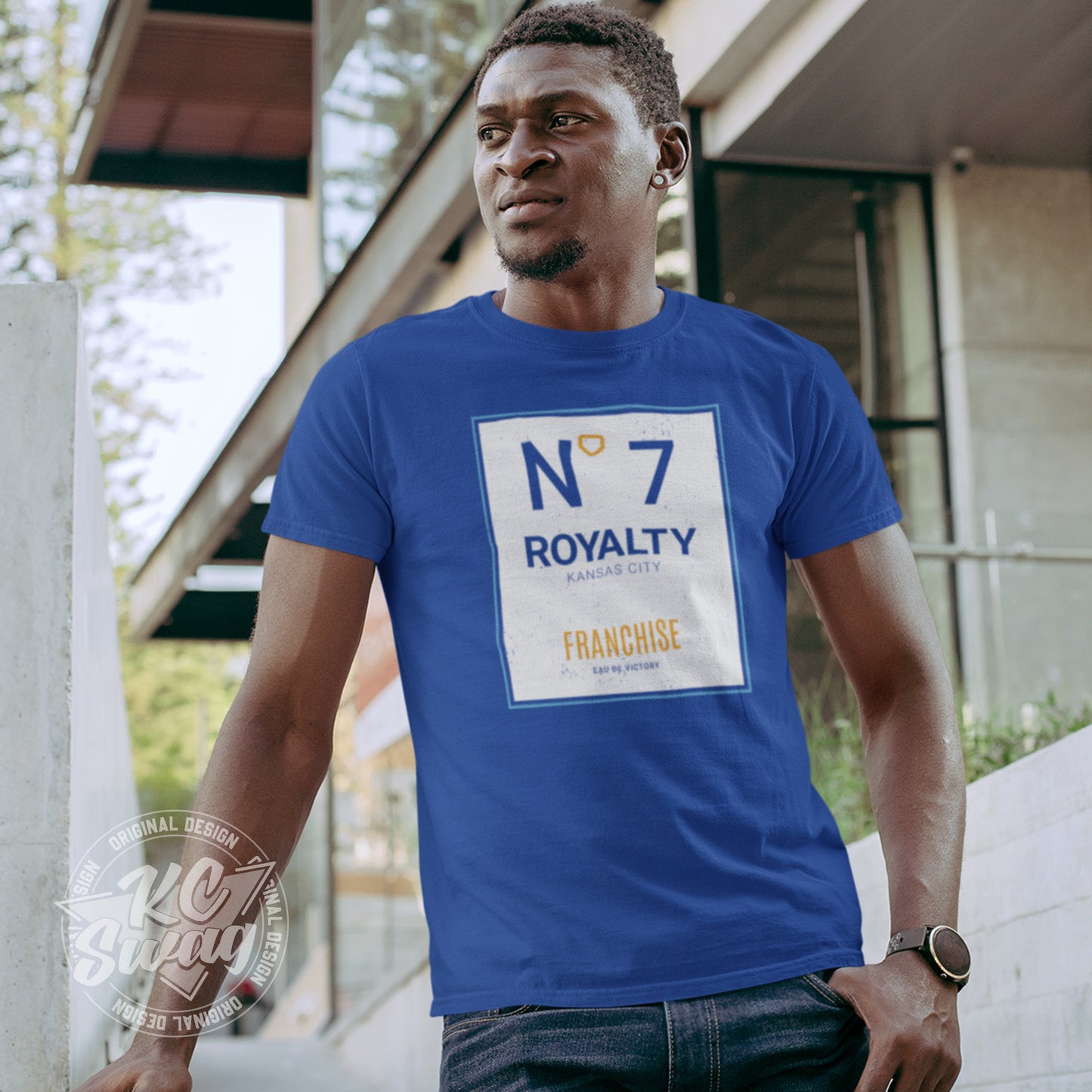 KC Swag - Kansas City Royals, Royalty Number 7 Franchise design on royal blue unisex t-shirt worn by male model leaning on railing outside of an apartment building