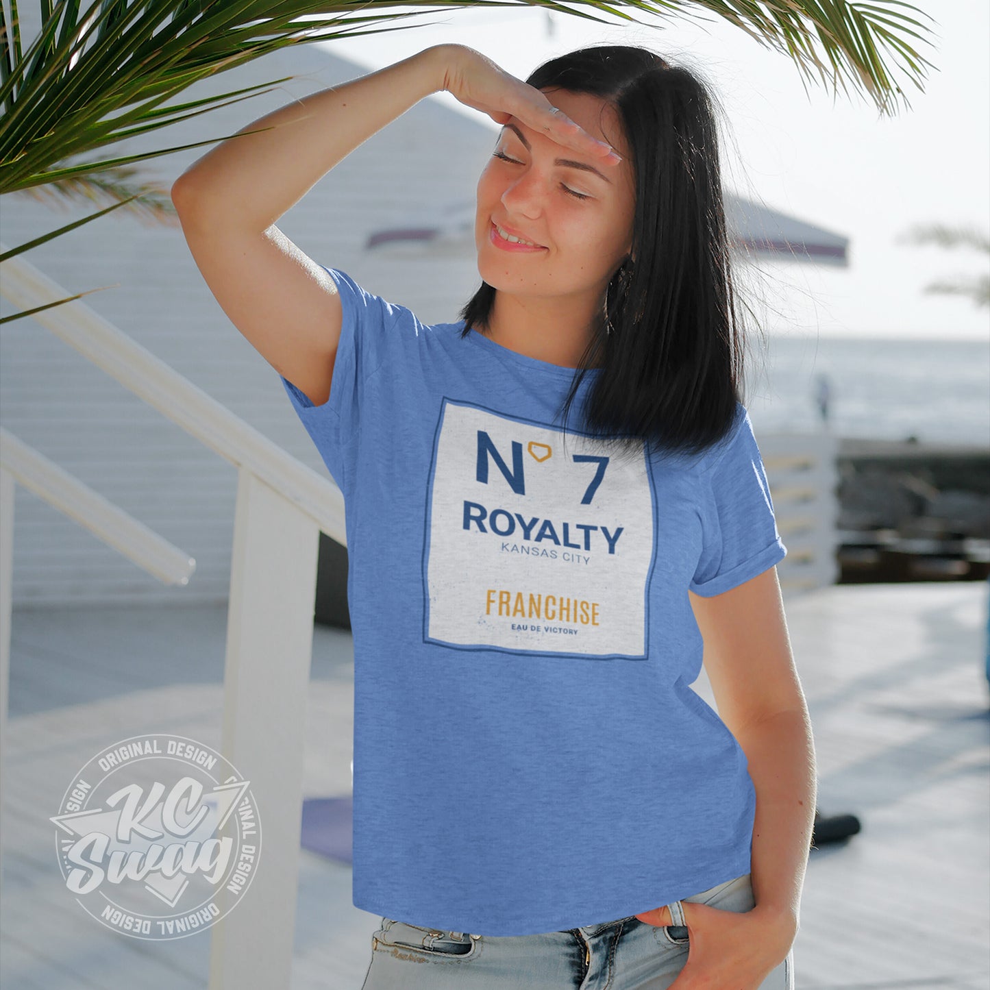 KC Swag - Kansas City Royals, Royalty Number 7 Franchise design on heather columbia blue unisex t-shirt worn by female model standing on a bright outdoor patio shading her eyes with her hand