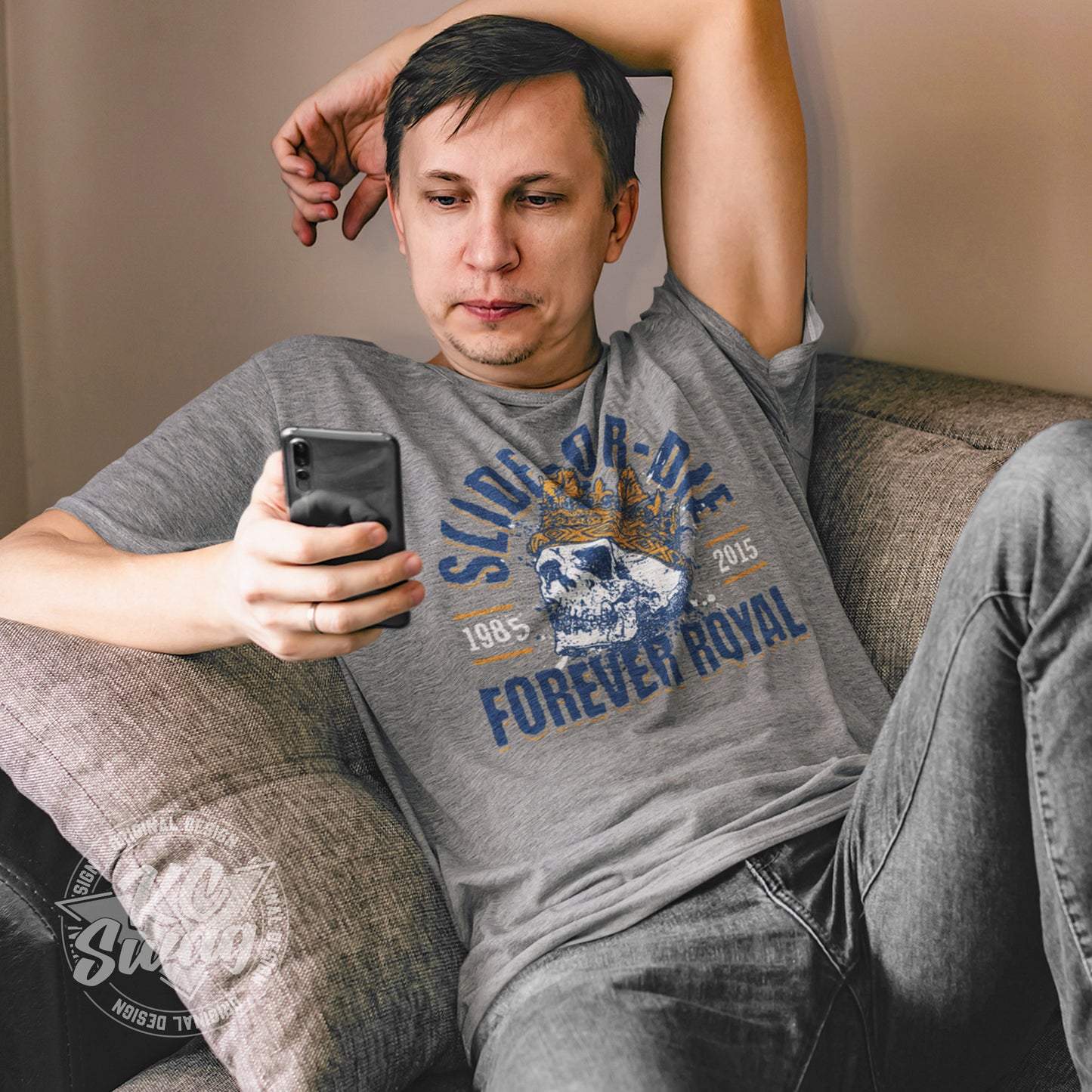 KC Swag - Kansas City Royals, Slide Or Die Forever Royal design on athletic heather grey unisex t-shirt worn by male model lounging on a couch playing with his smart phone