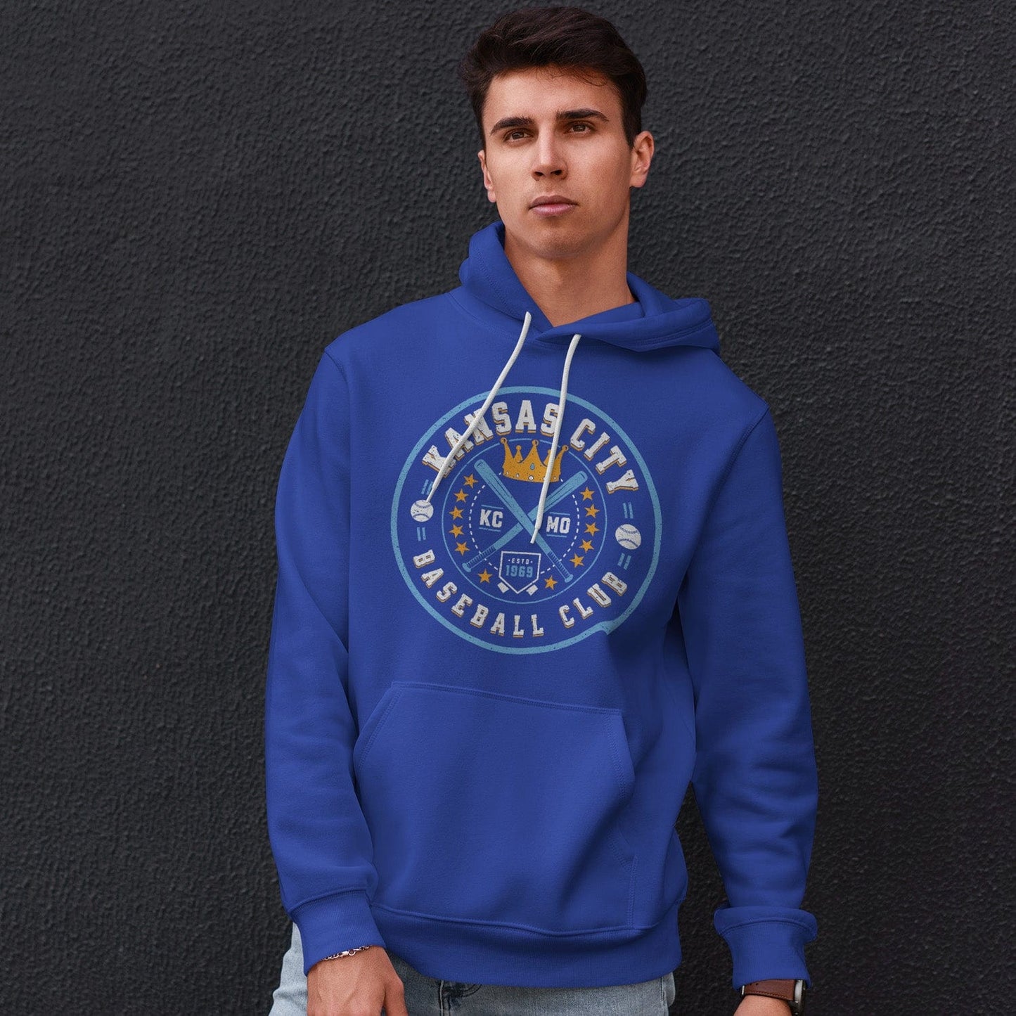 KC Swag Kansas City Royals powder, gold KC BASEBALL CLUB on royal blue fleece pullover hoodie worn by male model leaning against dark grey wall
