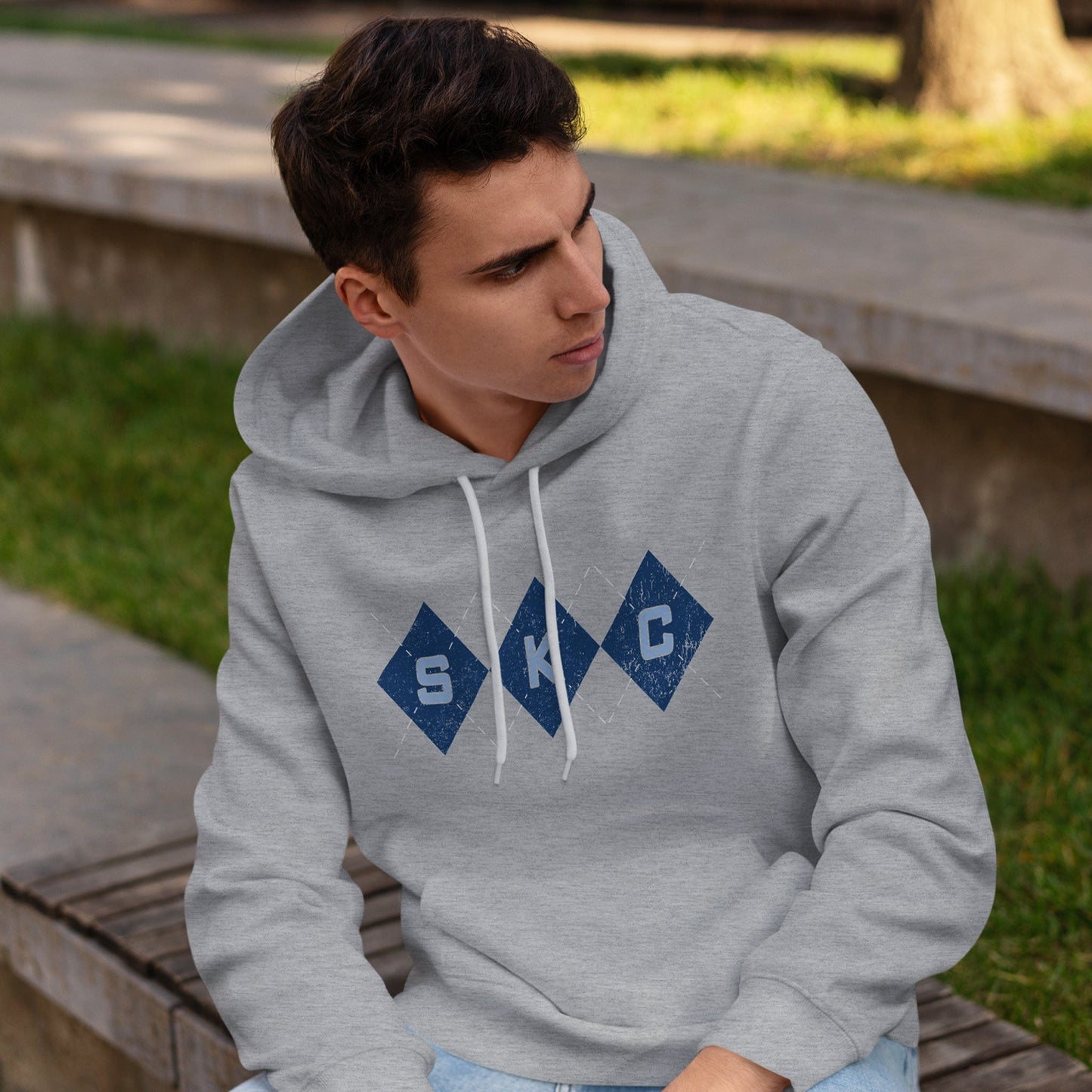 KC Swag Sporting Kansas City powder blue/navy/white SKC DIAMONDS on athletic heather grey fleece pull-over hoodie worn by male model sitting on bench in park
