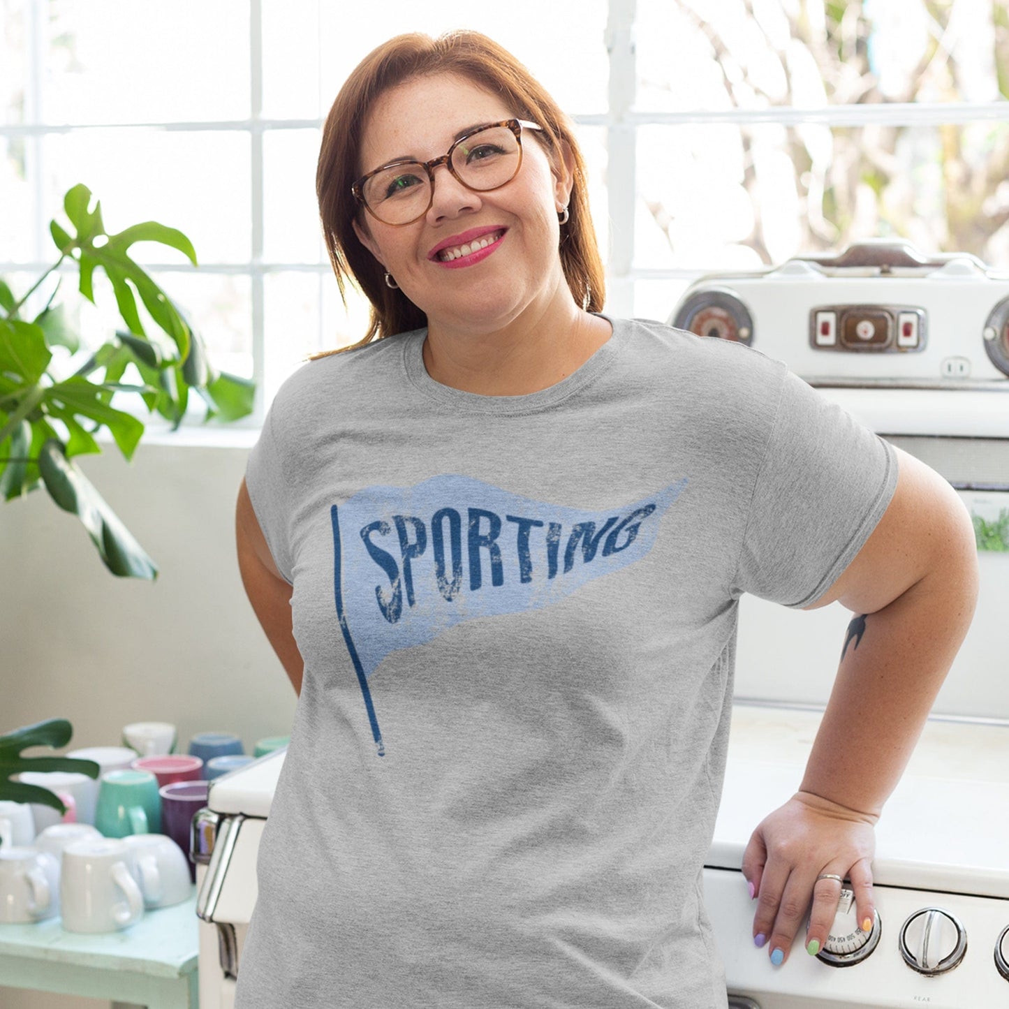 KC Swag Sporting Kansas City powder blue/navy SPORTING PENNANT on athletic heather grey t-shirt worn by female model in bright kitchen
