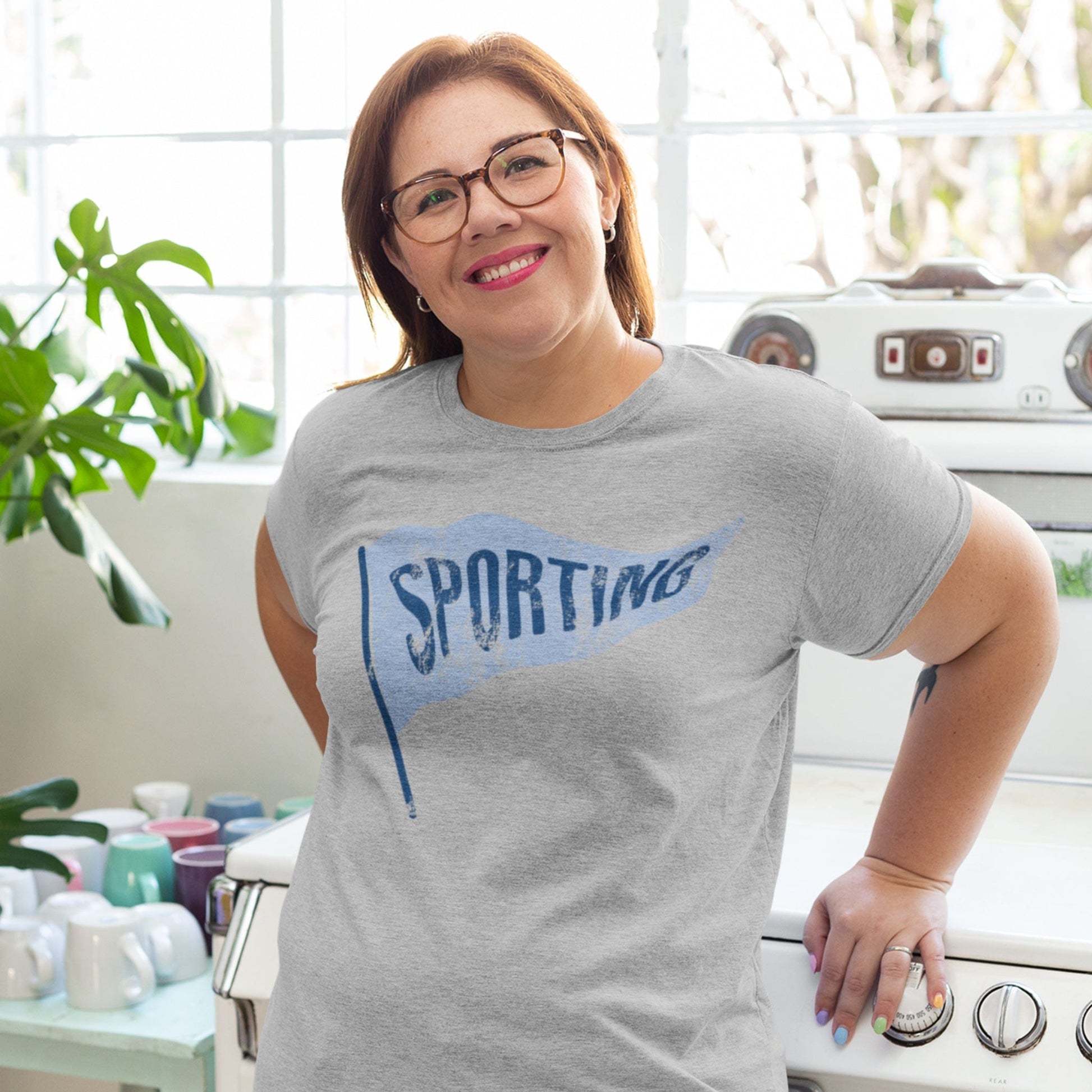 KC Swag Sporting Kansas City powder blue/navy SPORTING PENNANT on athletic heather grey t-shirt worn by female model in bright kitchen