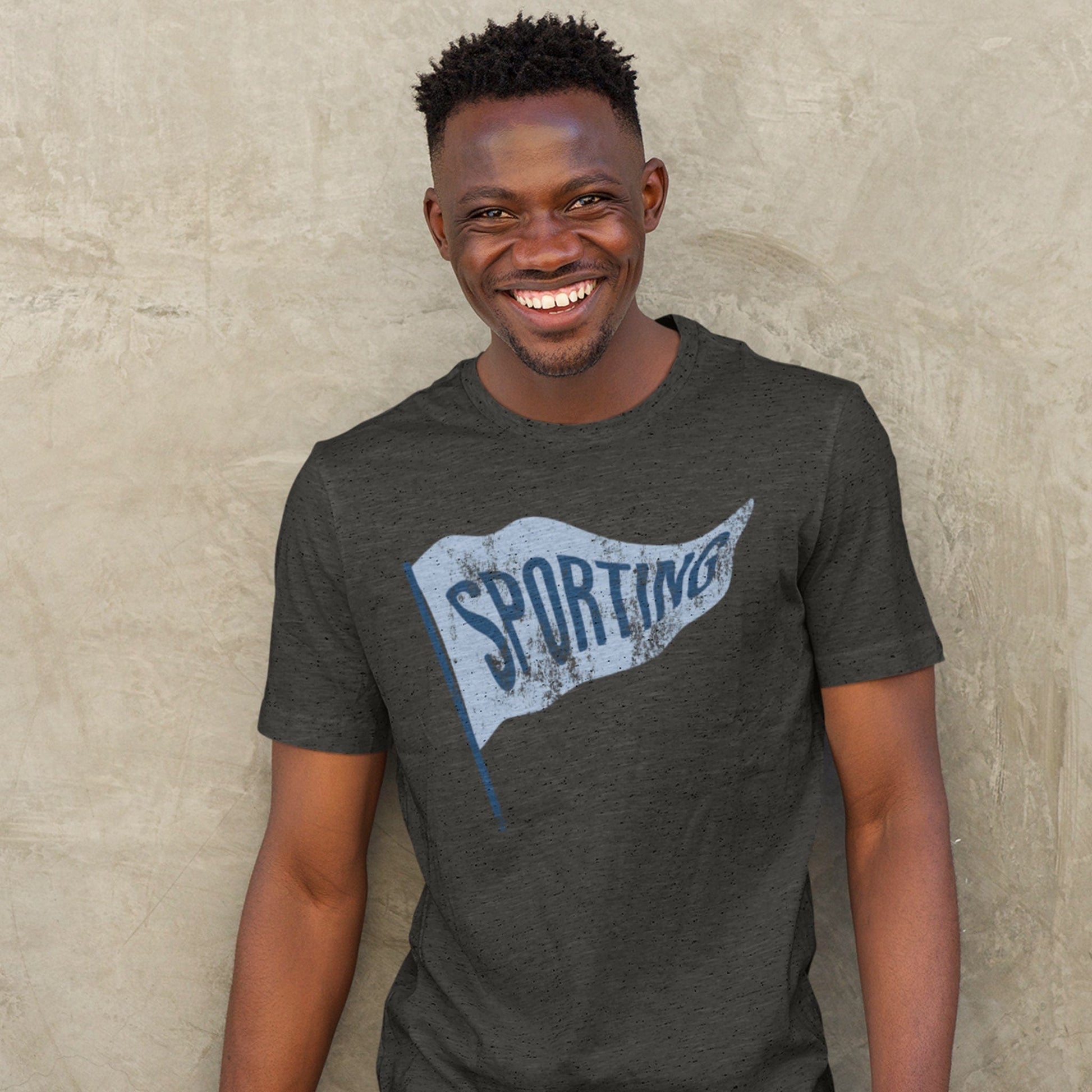 KC Swag Sporting Kansas City powder blue/navy SPORTING PENNANT on dark heather grey t-shirt worn by male model against stone wall