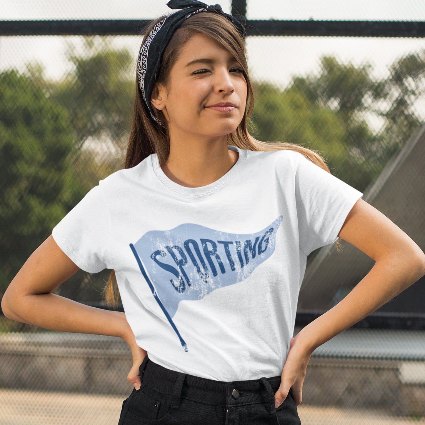 KC Swag Sporting Kansas City powder blue/navy SPORTING PENNANT on white t-shirt worn by bandana wearing dark-haired female model standing in front of chain fence in park