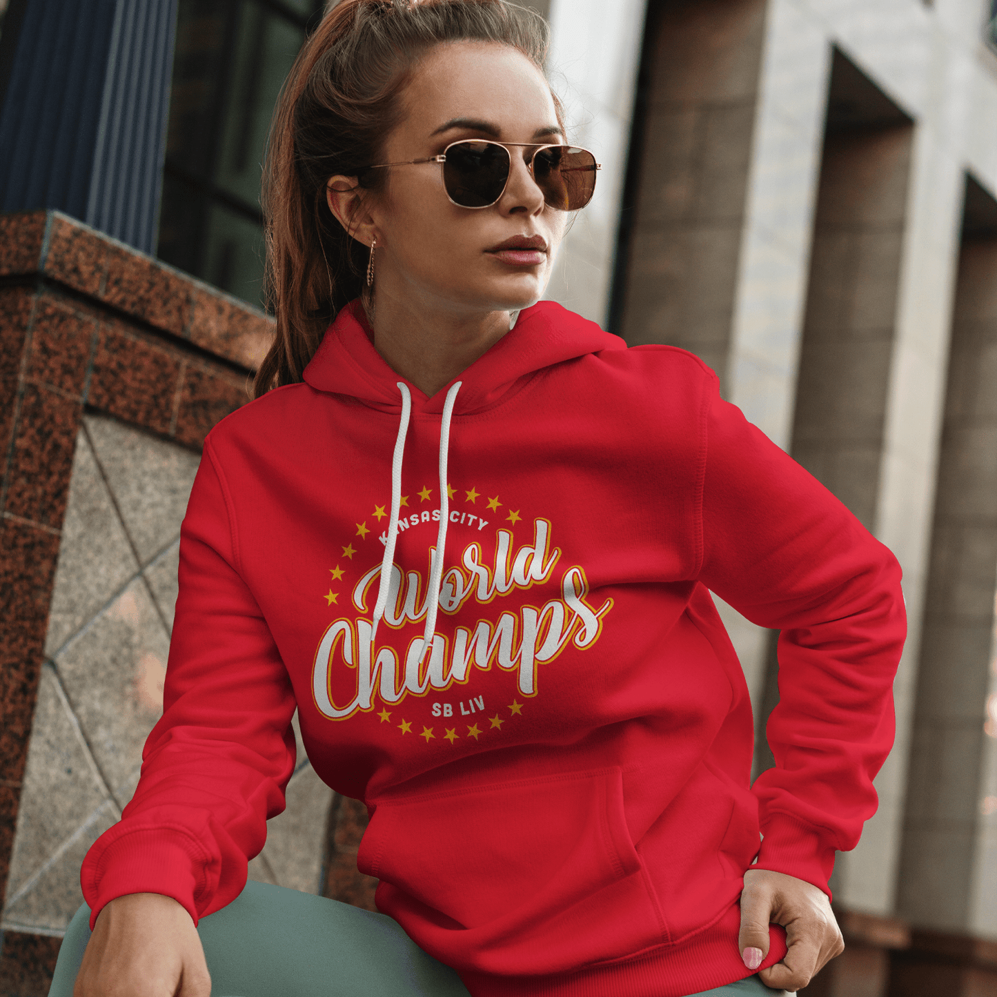 KC Swag Kansas City WORLD CHAMPS SBLIV on red fleece pullover hoodie worn by female model sitting on steps of downtown building