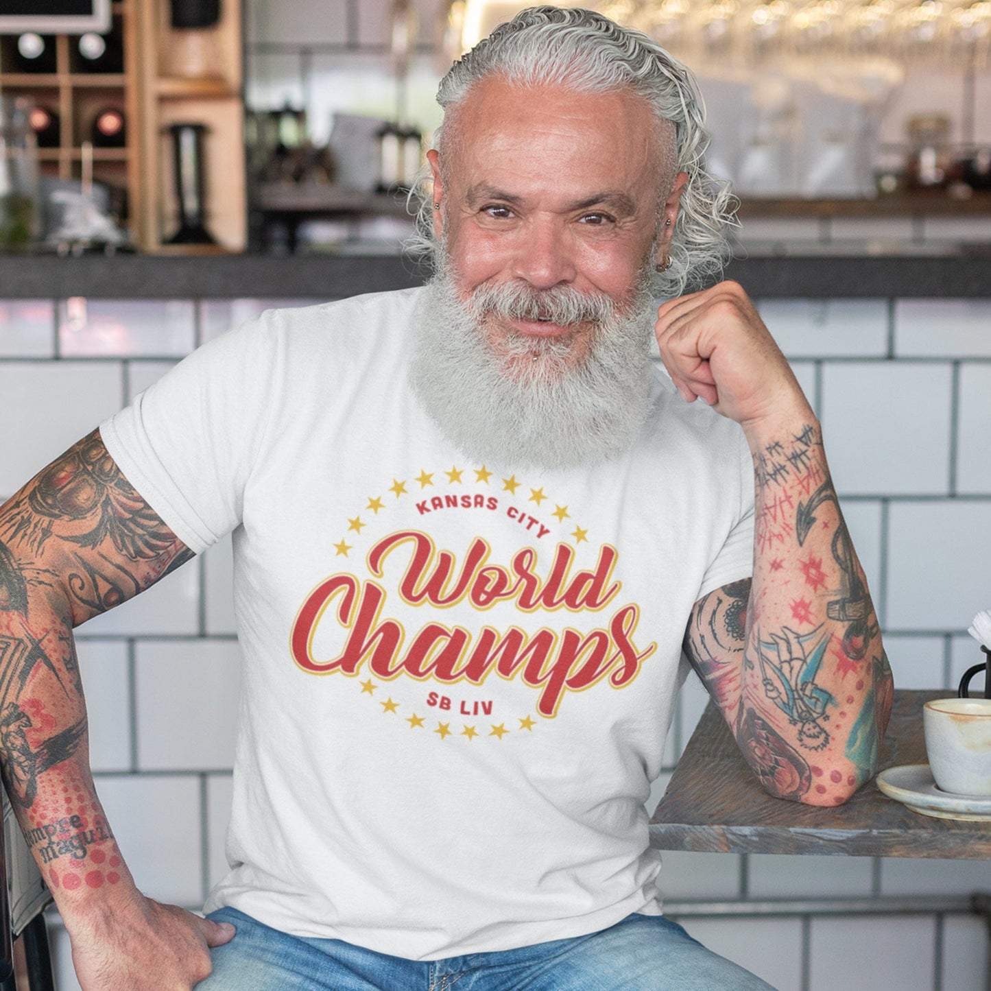 KC Swag Kansas City Chiefs yellow/red WORLD CHAMPS set in ring of stars on white t-shirt worn by grey bearded male model sitting in cafe