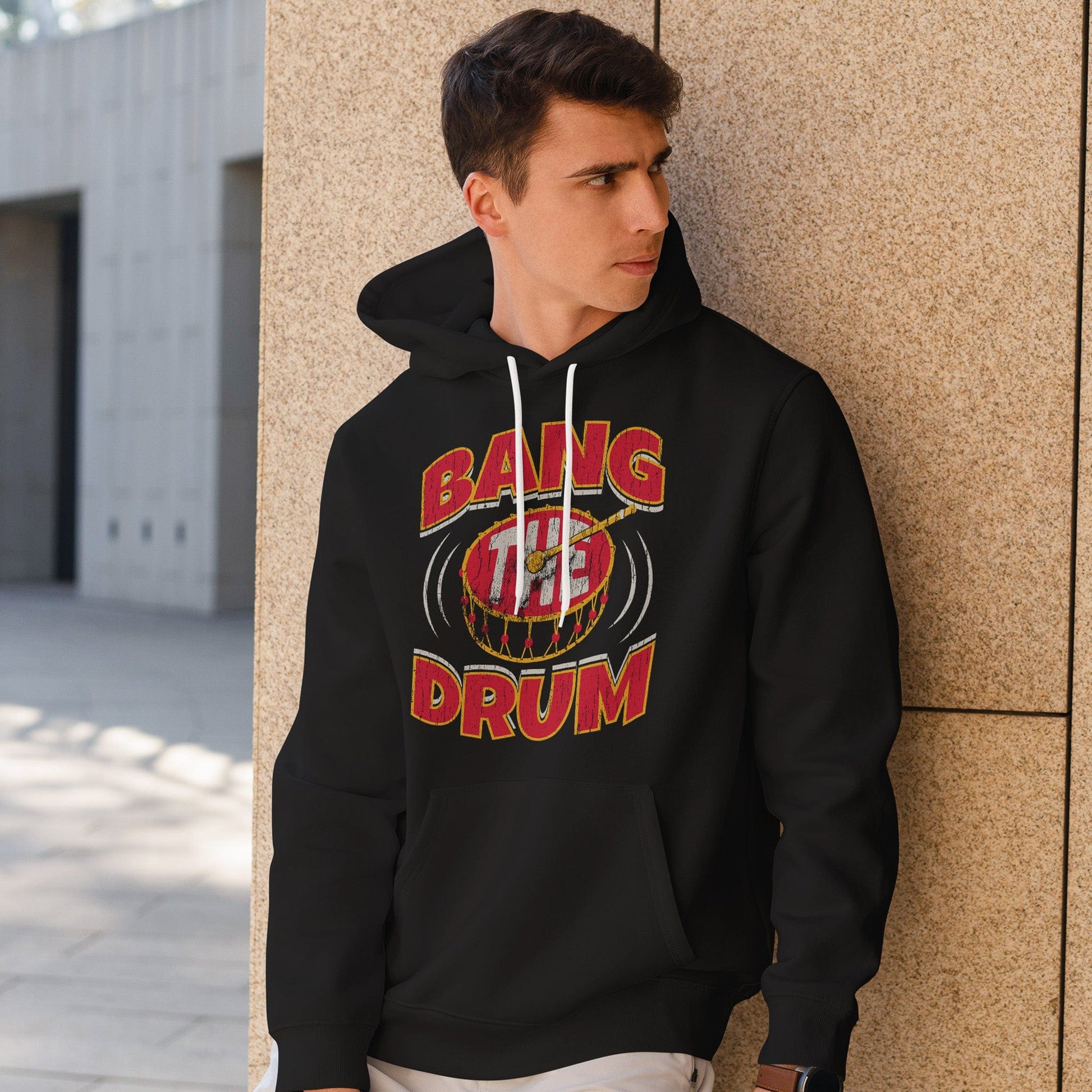 KC Swag | Kansas City Chiefs white/red/gold BAG THE DRUM on black sponge-fleece pullover hoodie worn by male model leaning against a stone wall in outdoor plaza