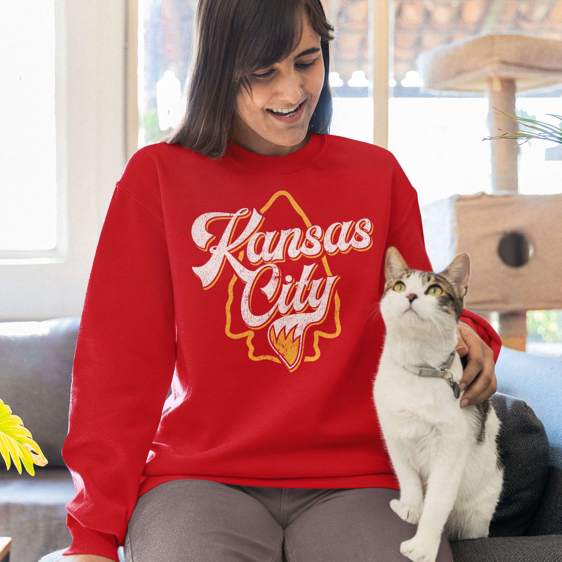 KC Swag Kansas City Chiefs Distressed White & Gold Wolftail KC on a Red Crewneck Sweatshirt worn by a female model sitting on a couch petting a cat