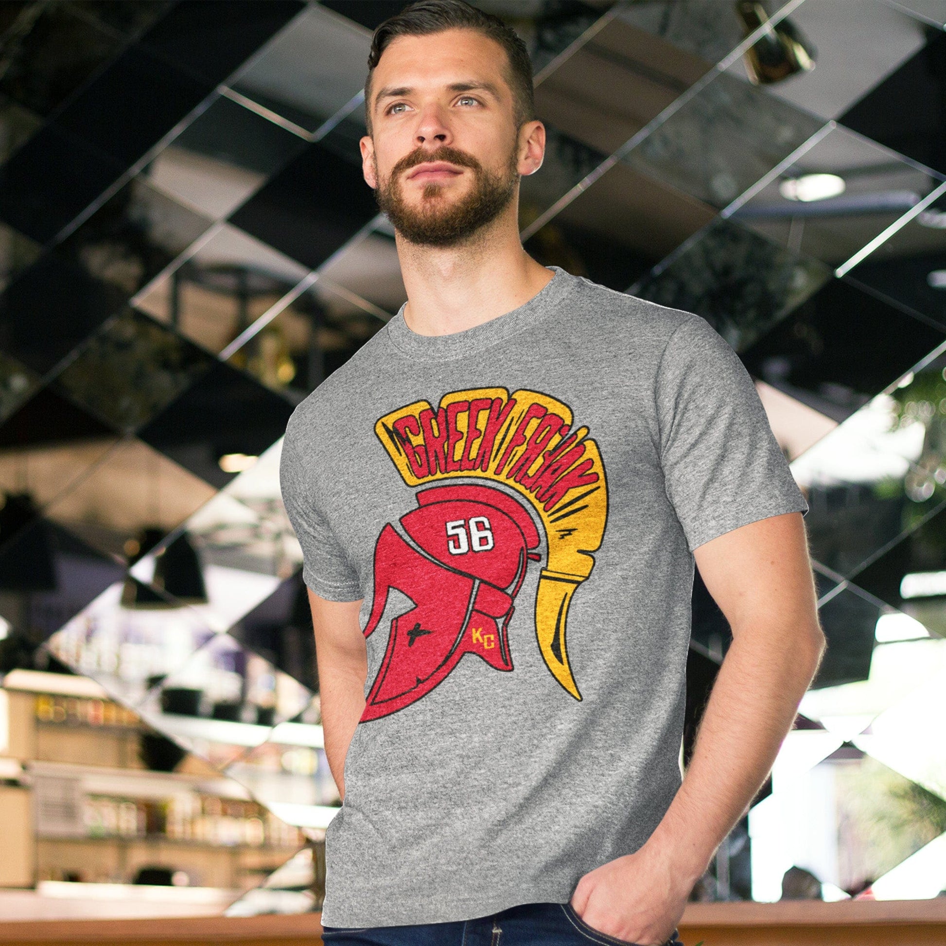 KC Swag | Kansas City Chiefs gold & red GREEK FREAK 56 on a trojan helmet on athletic heather gray unisex t-shirt worn by male model standing in front of a mosaic mirrored walled