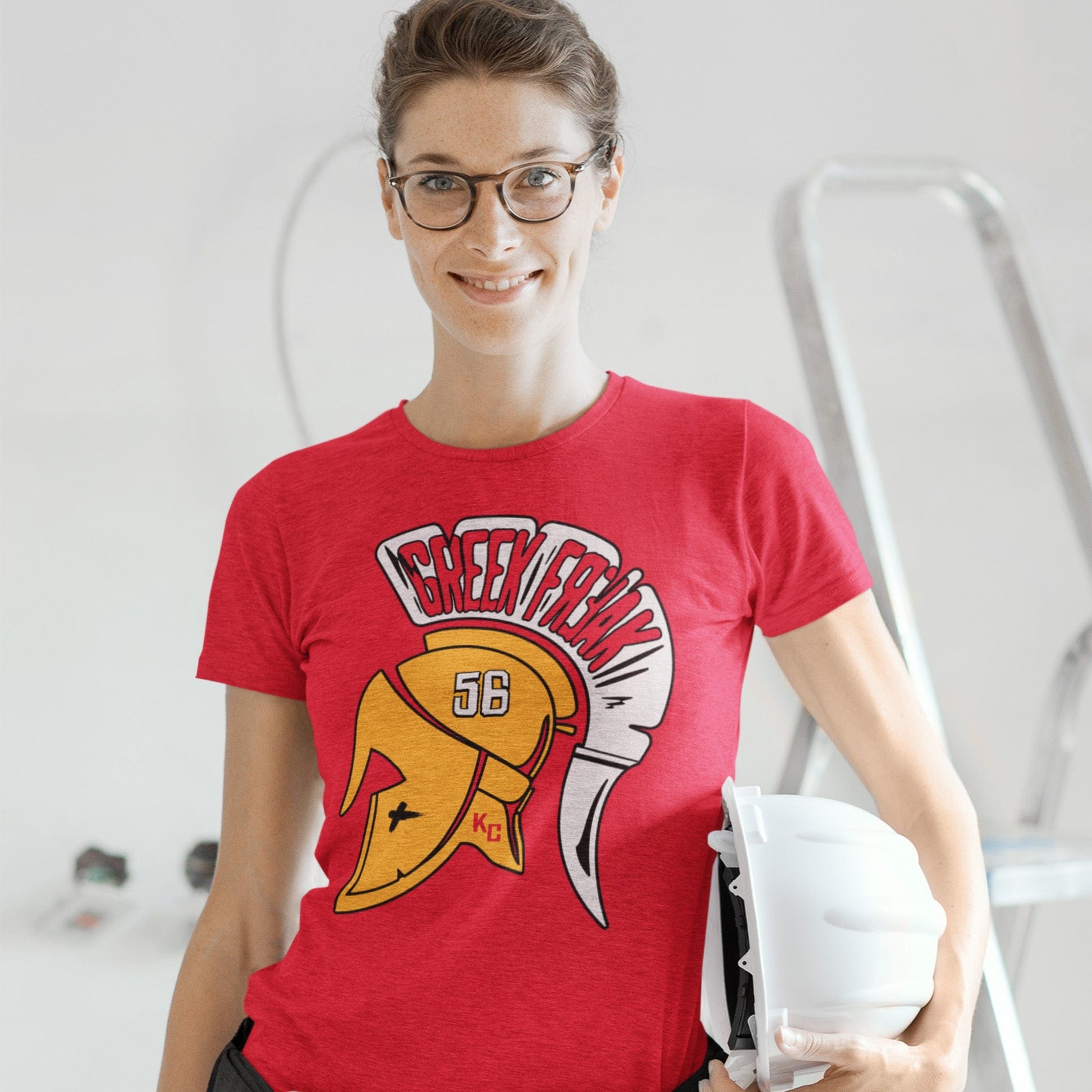 KC Swag | Kansas City Chiefs white, gold & red GREEK FREAK 56 on a trojan helmet on heather red unisex t-shirt worn by female model holding a hard hat standing in a home remodel zone