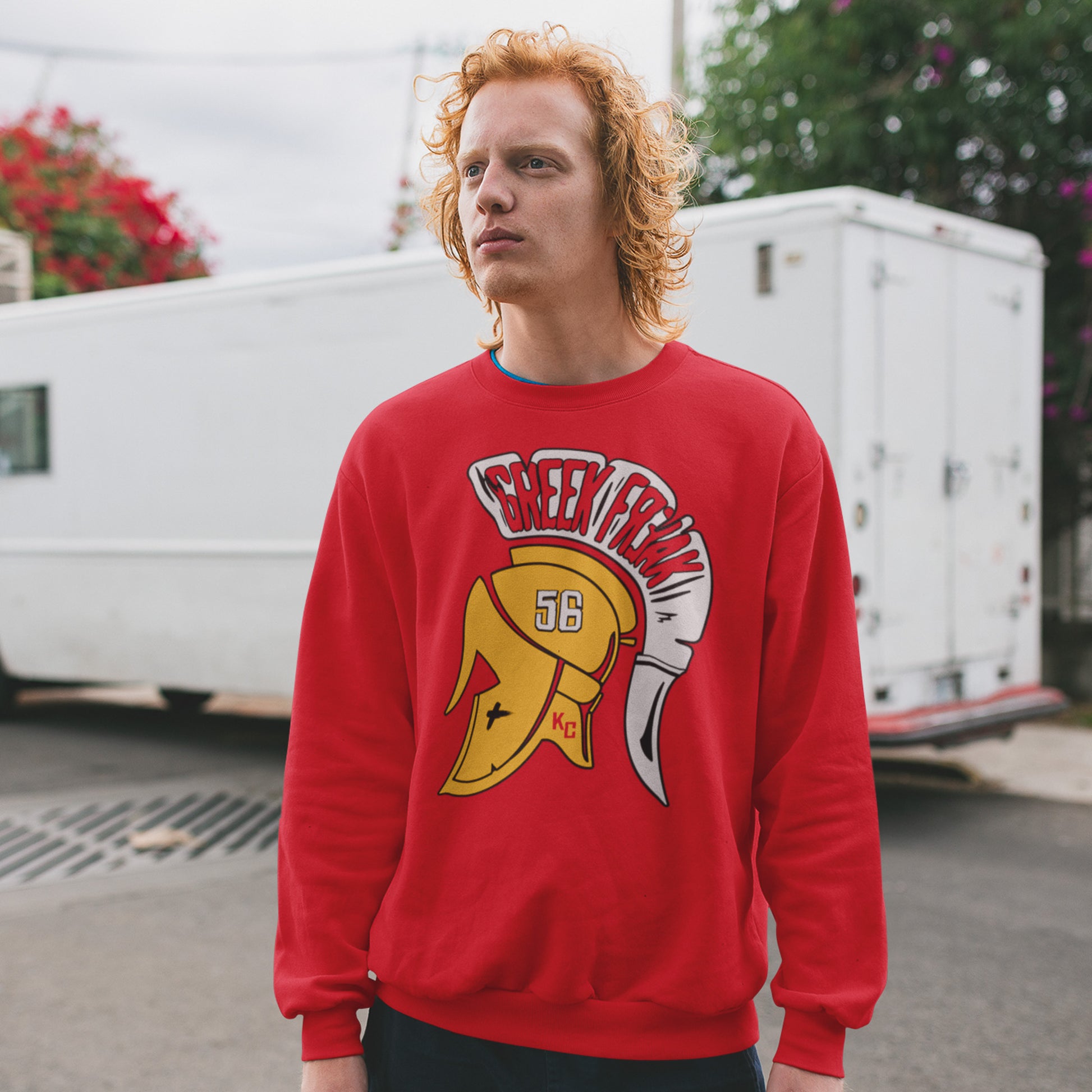 KC Swag Kansas City Chiefs White & Gold Greek Freak (with Trojan Helmet) on a Red Crewneck Sweatshirt worn by ginger-haired male model standing in a parking lot in front of a white delivery truck
