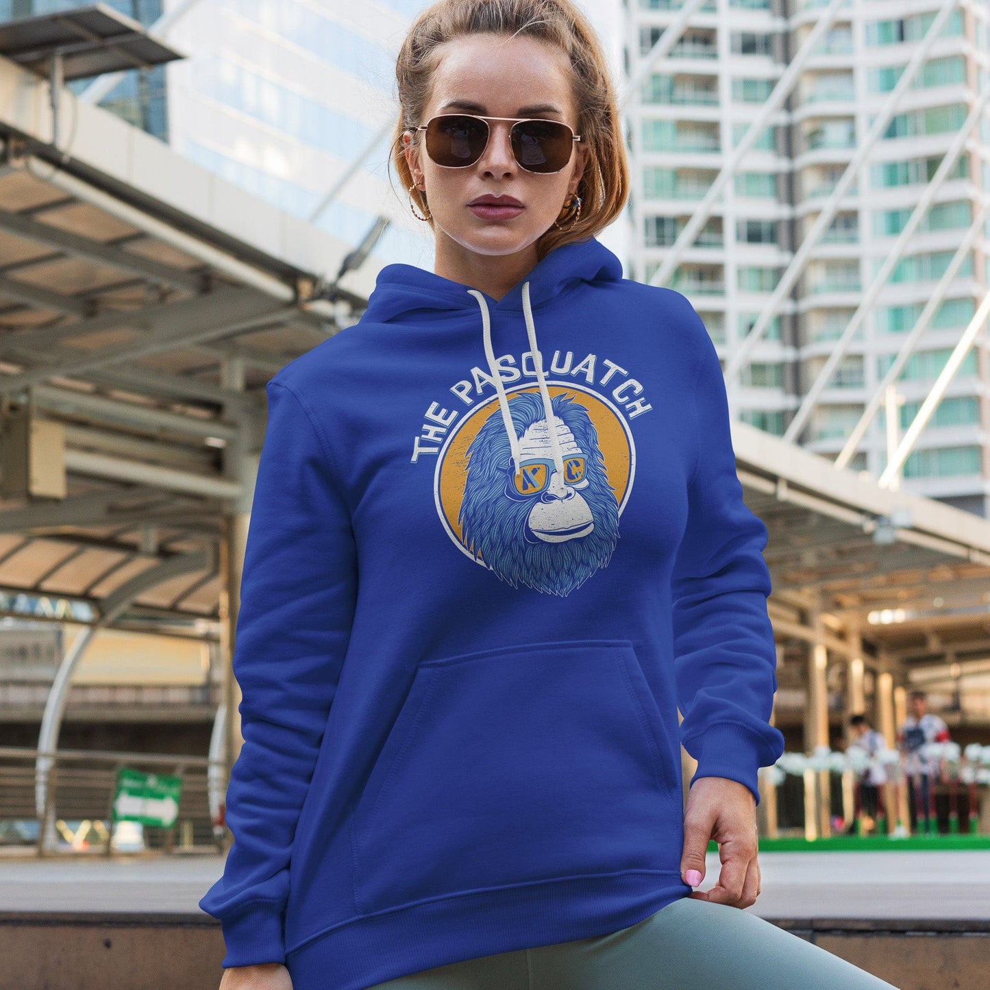 KC Swag | Kansas City Royals gold/blue/white KC PASQUATCH on blue sponge-fleece pullover hoodie worn by female model standing outside of downtown building