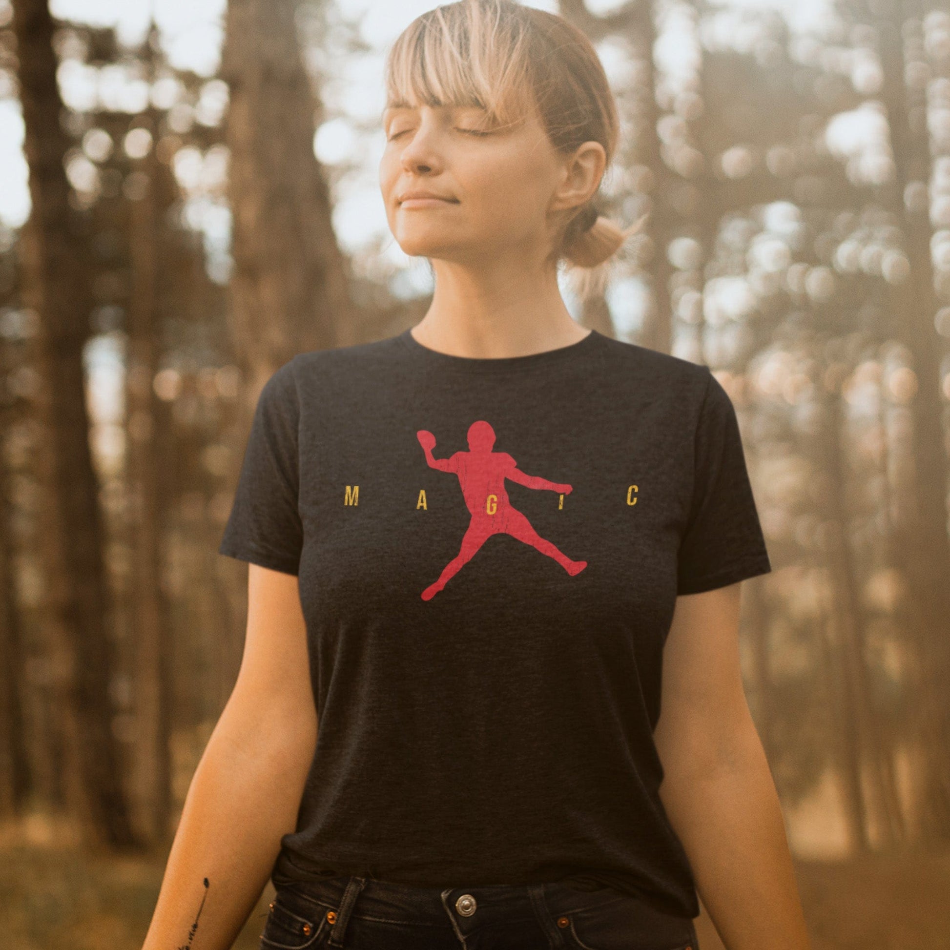 KC Swag | Kansas City Chiefs red & gold MAGIC AIR MAHOMIE on a heather black unisex t-shirt worn by a female model basking in the sun in a forrest setting