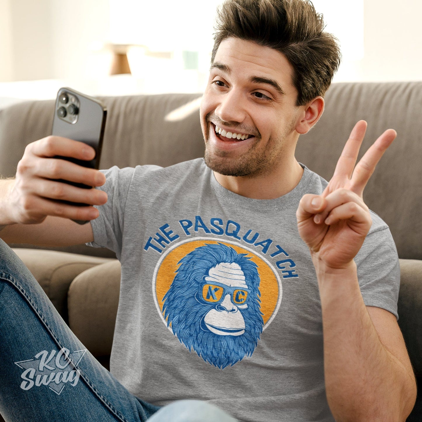 KC Swag Kansas City Royals KC PASQUATCH on athletic heather grey unisex t-shirt worn by male model giving the 'peace-sign' while face-timing on his phone