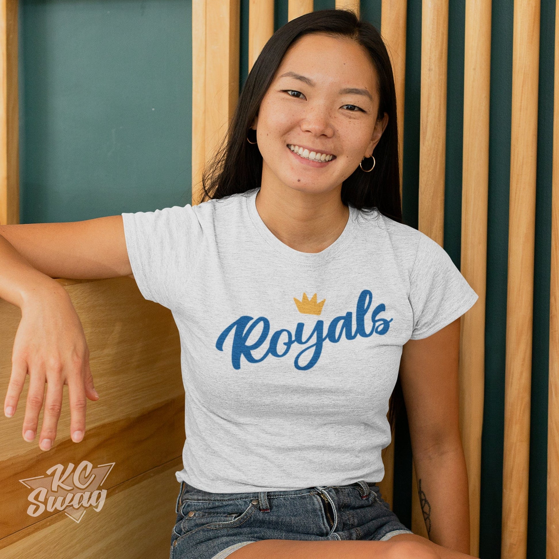 KC Swag Kansas City Royals ROYALS CROWN on ash grey unisex t-shirt worn by female model sitting in front of a wood slat wall