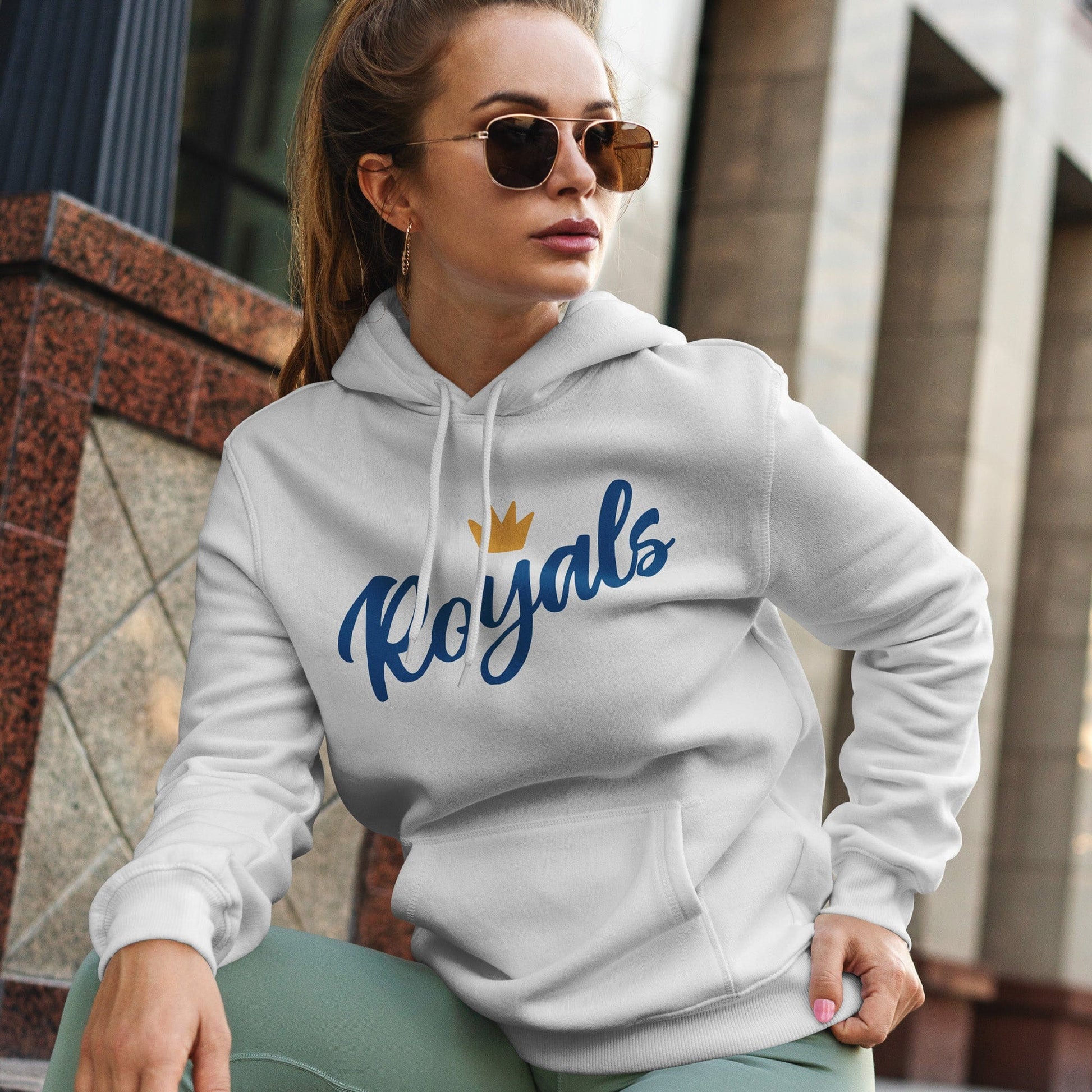 KC Swag | Kansas City Royals blue/gold FLOWER CROWN on white sponge-fleece pullover hoodie worn by female model stiing in front of old downtown building