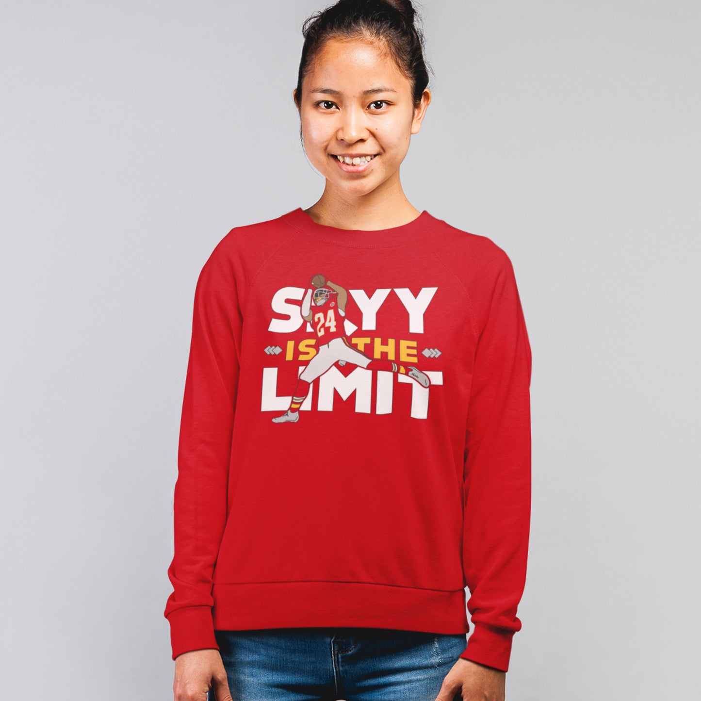 KC Swag Kansas City Chiefs White & Gold Skyy Is The Limit (with football player) on a Red Crewneck Sweatshirt worn by a smiling female model standing in front of a gray studio wall