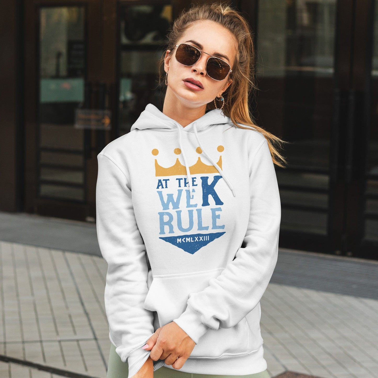 KC Swag | Kansas City Royals blue/gold AT THE K WE RULE on white sponge-fleece pullover hoodie worn by female model standing outside of shopping mall entrance