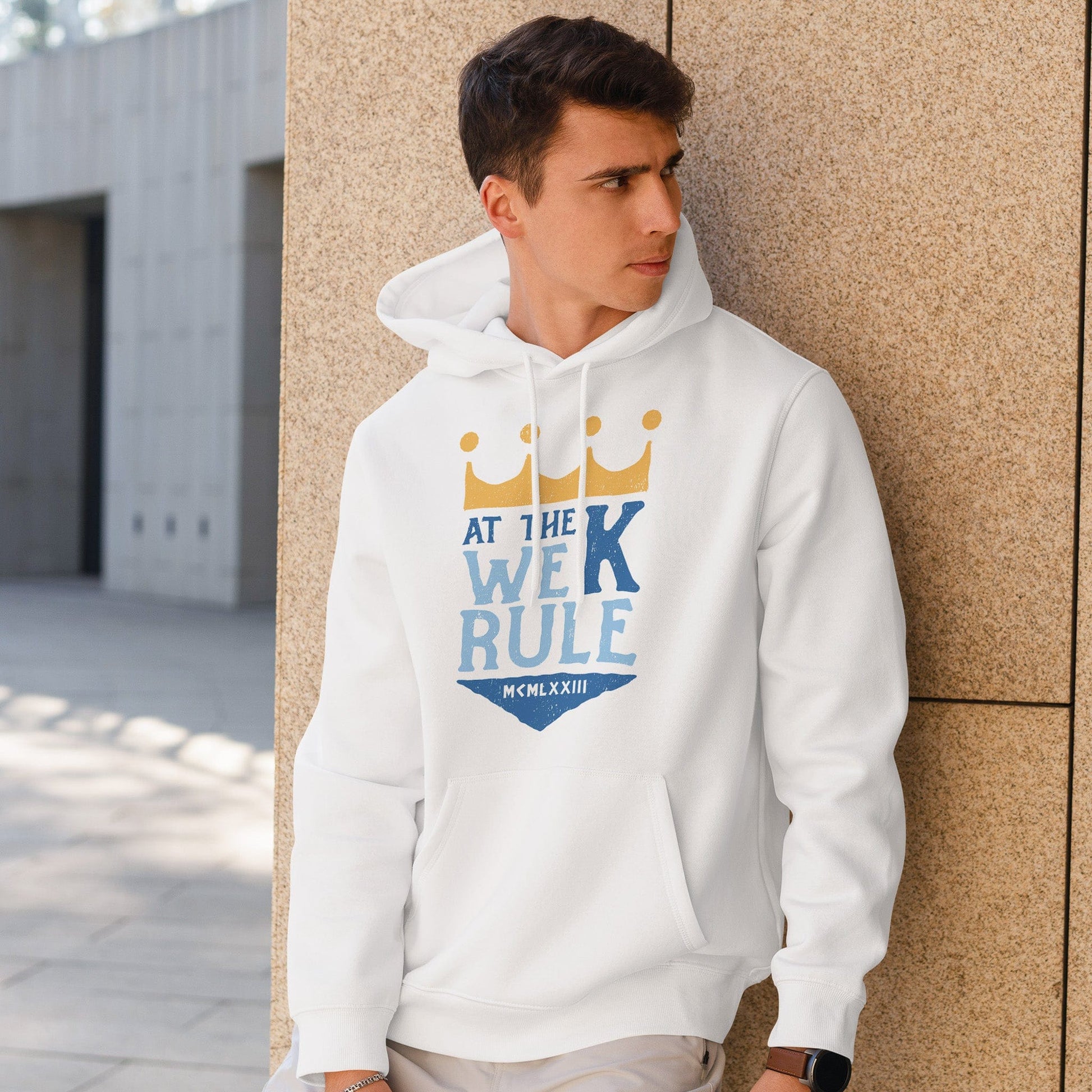 KC Swag | Kansas City Royals blue/gold AT THE K WE RULE on white sponge-fleece pullover hoodie worn by male model leaning against stone wall in outdoor plaza